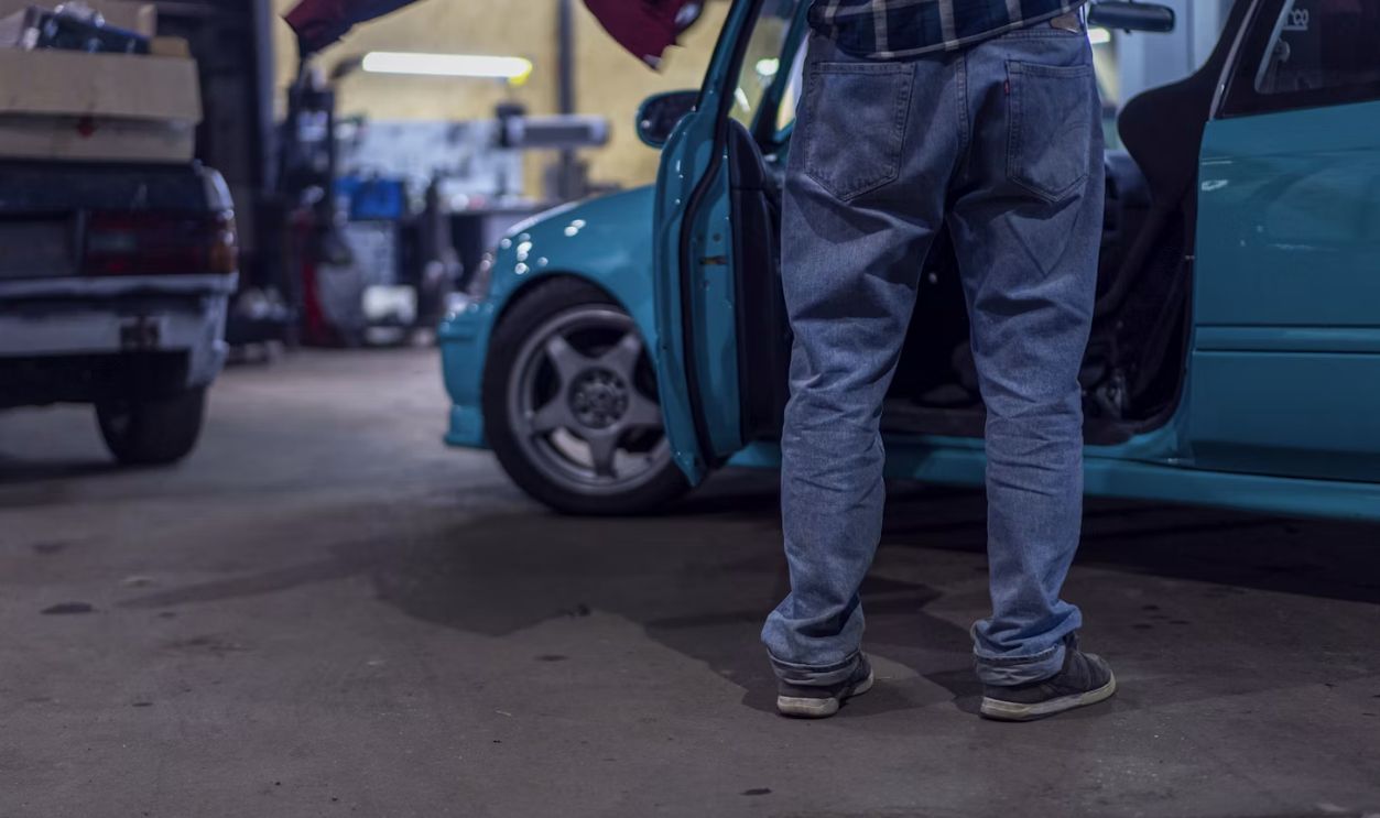 man in blue denim jeans and black leather boots standing beside blue car during daytime
