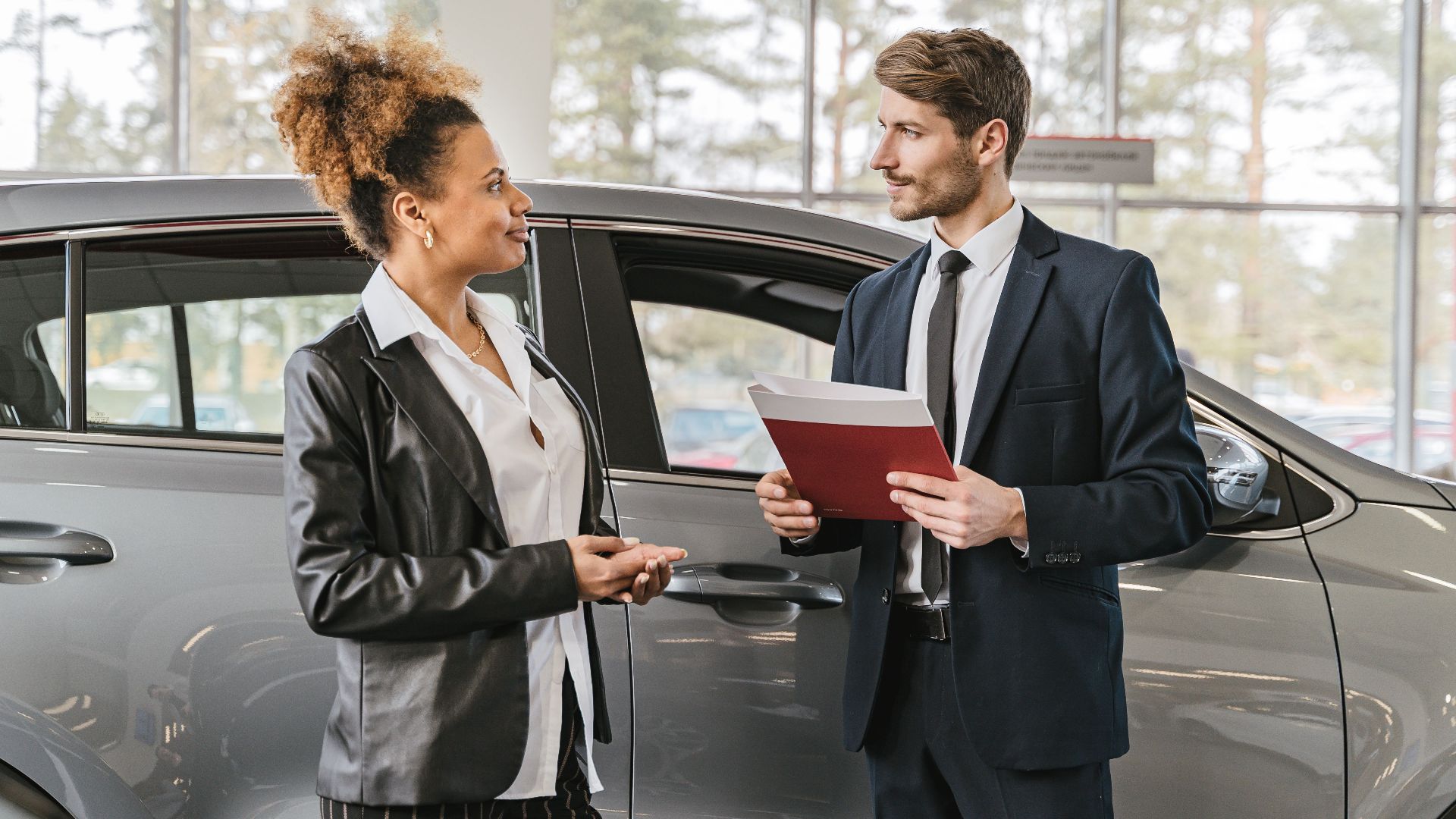 A woman discussing car purchase with a dealer inside a car dealership showroom.