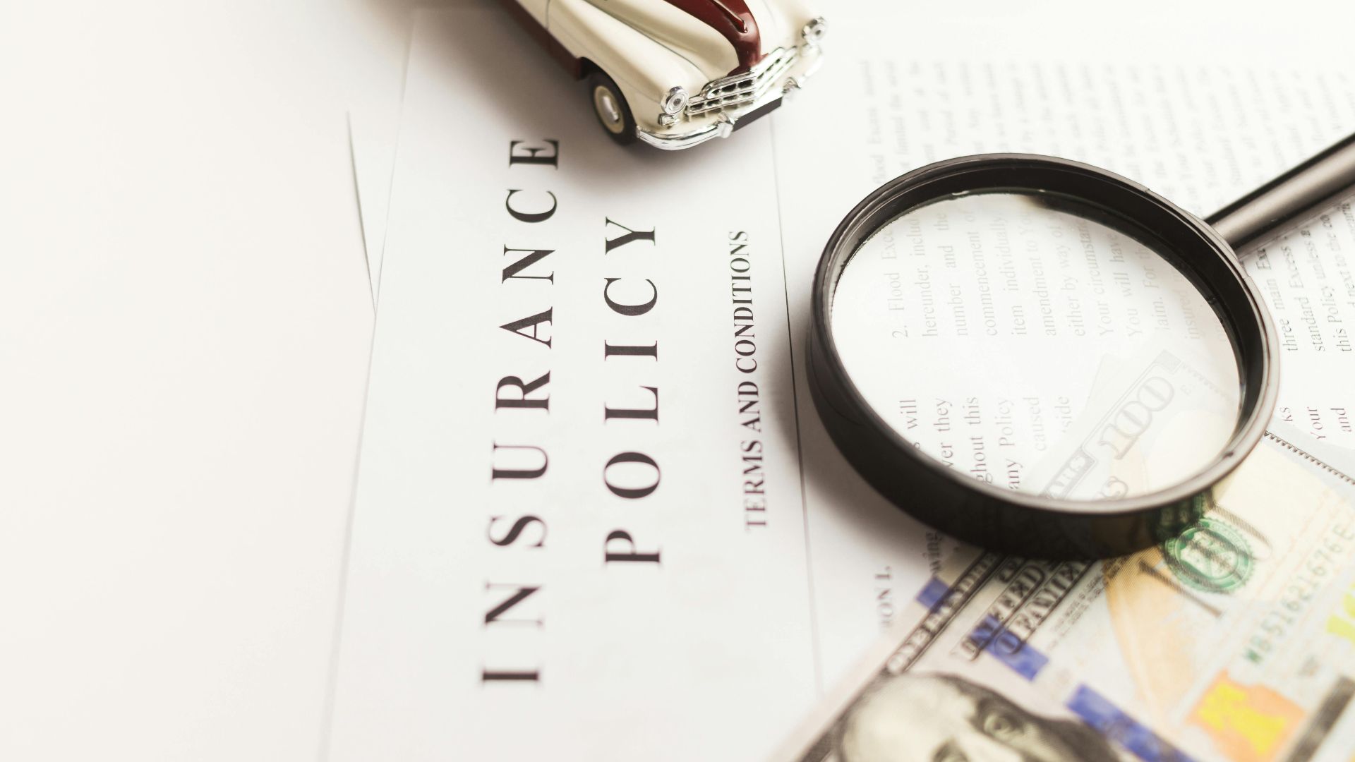 Close-up image of an insurance policy with a magnifying glass, money, and toy car.