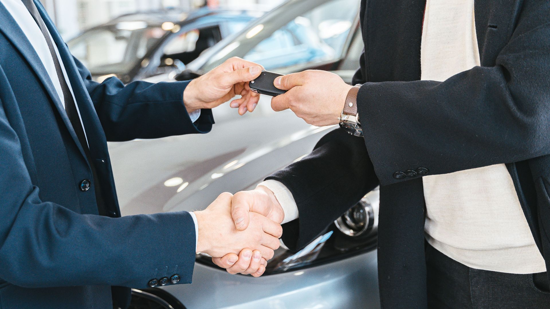 Two businessmen shaking hands and exchanging car keys in a dealership. Symbolizes a successful deal.