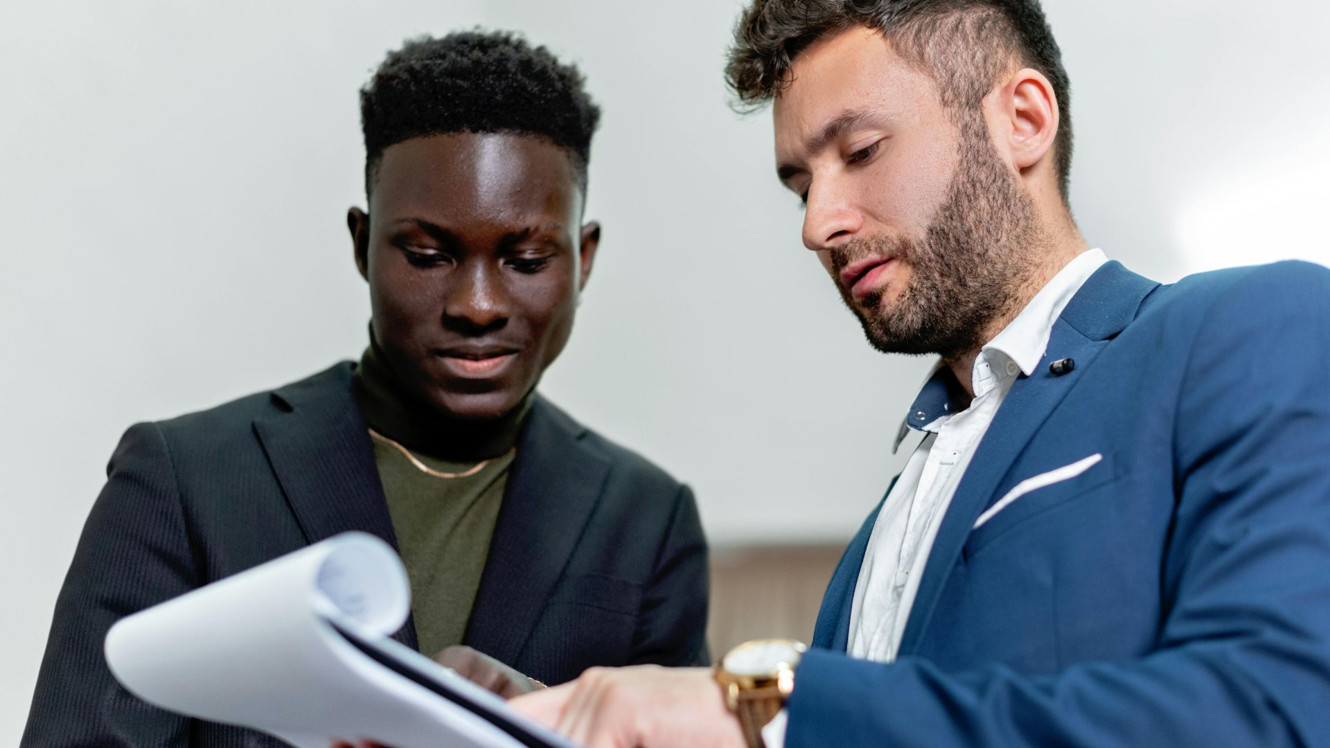 Two businessmen in suits discuss important documents in an office setting.