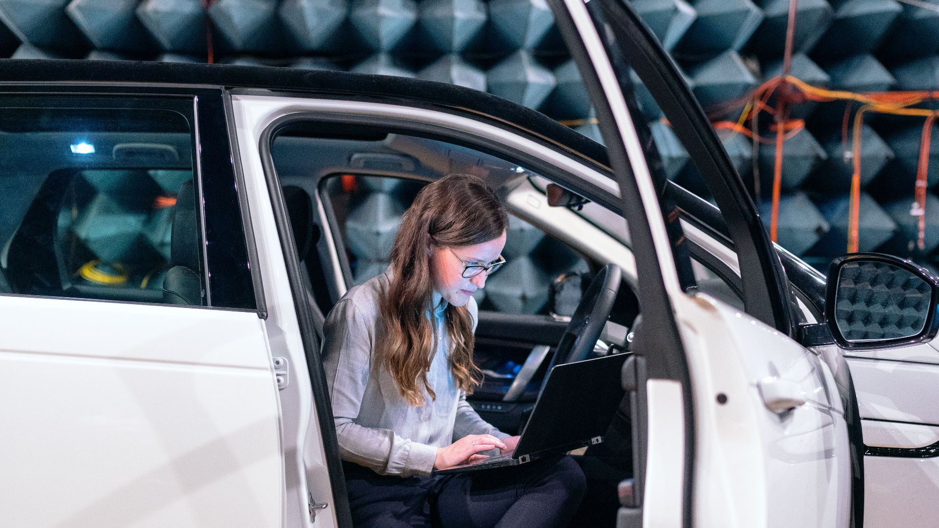 Sound engineer working on a laptop inside a car for acoustic testing in an anechoic chamber.