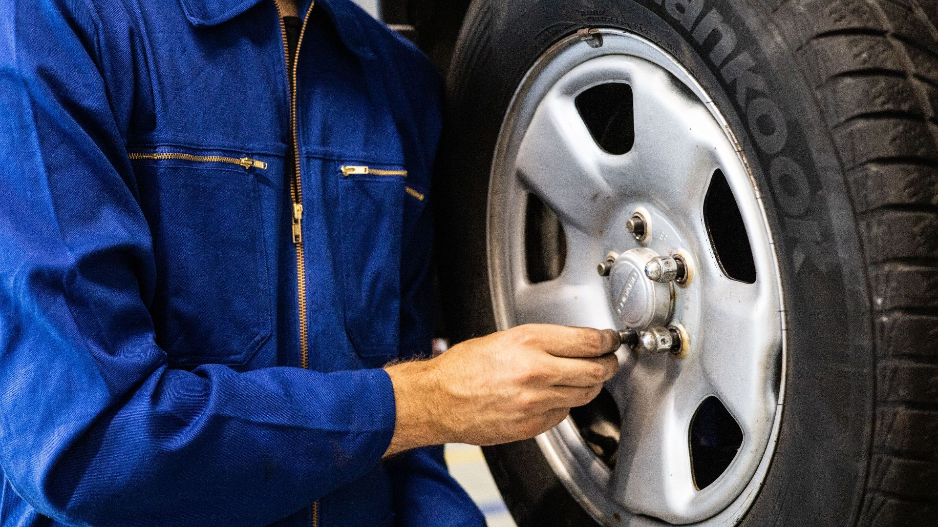 Mechanic in blue coveralls inspecting a car tire in an auto repair workshop.