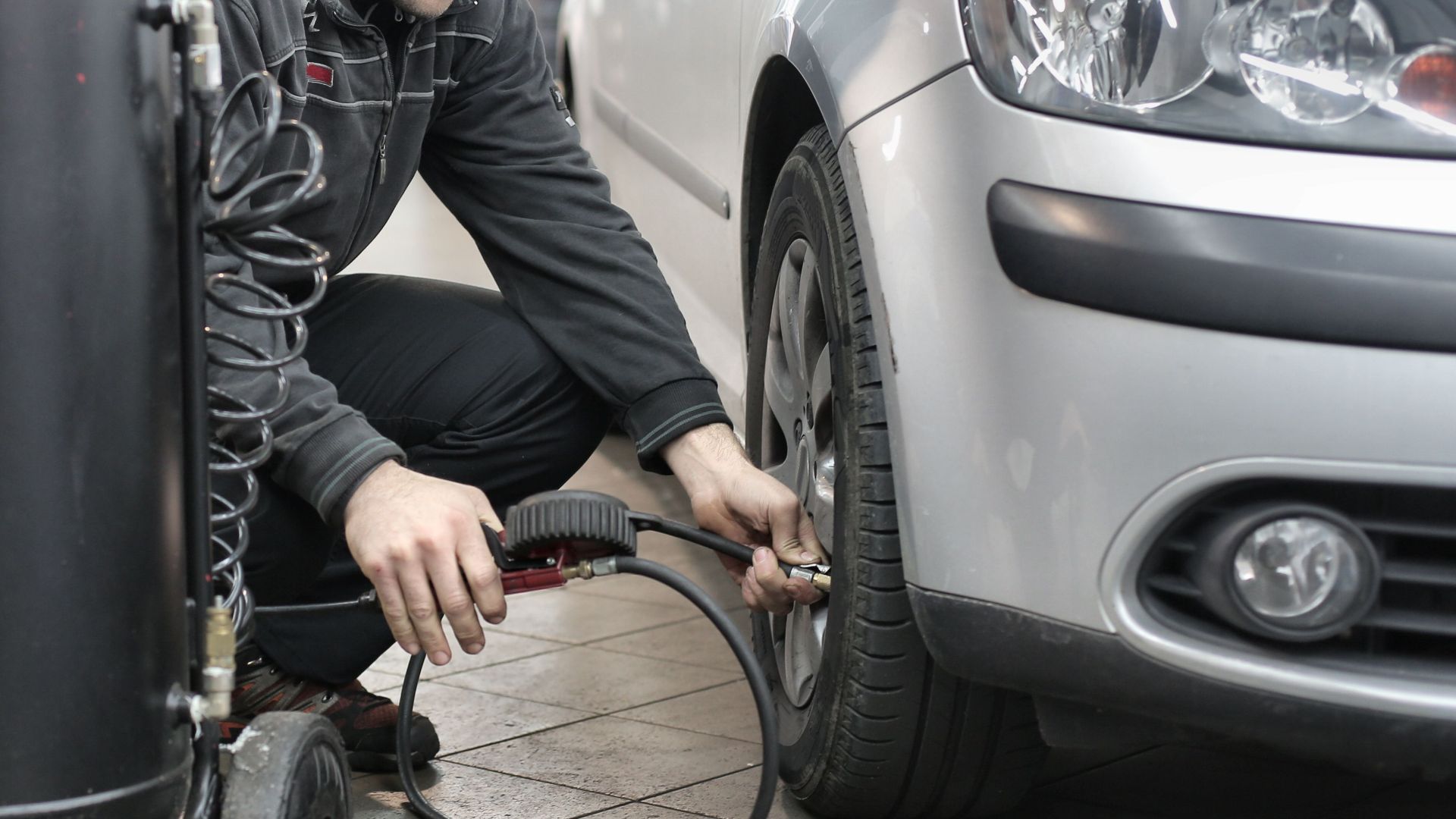 Mechanic inspecting and adjusting tire pressure in an auto repair shop.