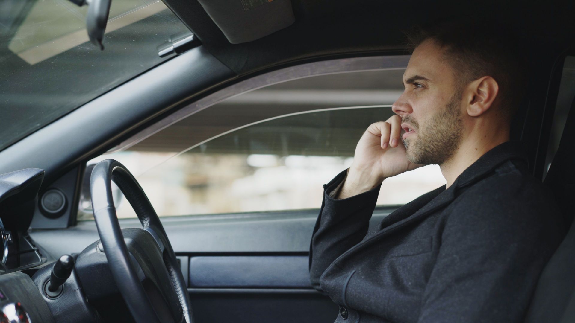 Focused man talking on smartphone in a car during the day, highlighting modern communication.