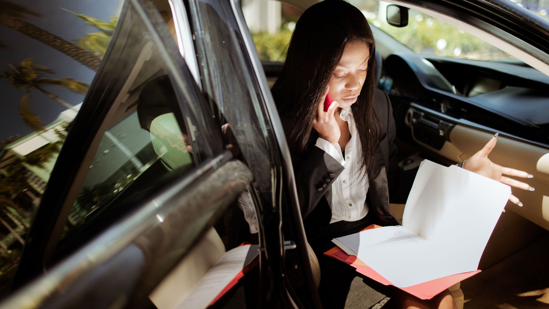 A businesswoman multitasking with phone and documents while seated in a car.