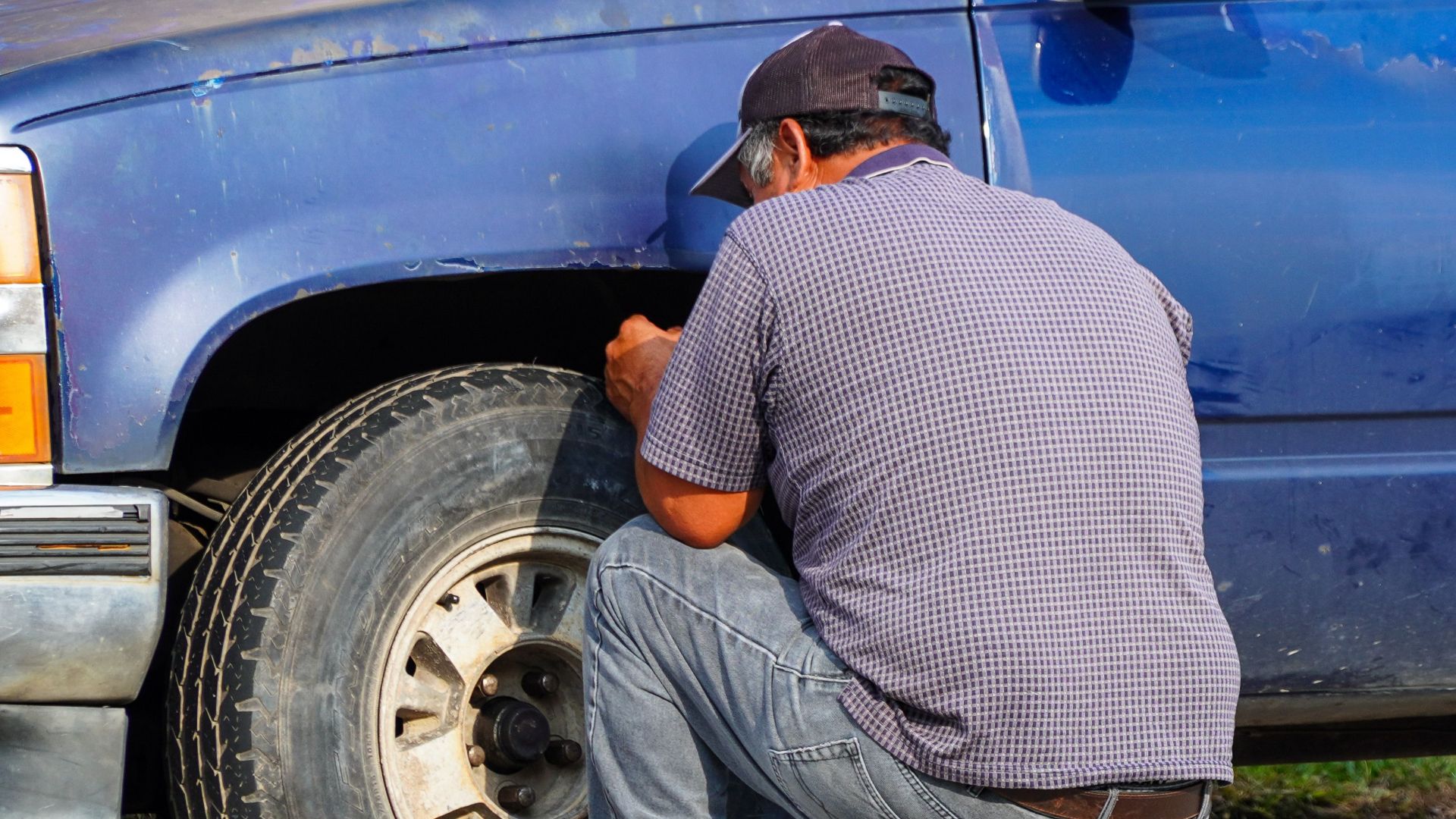 A man attentively repairing a flat tire on a blue truck in sunny Houston, Texas.