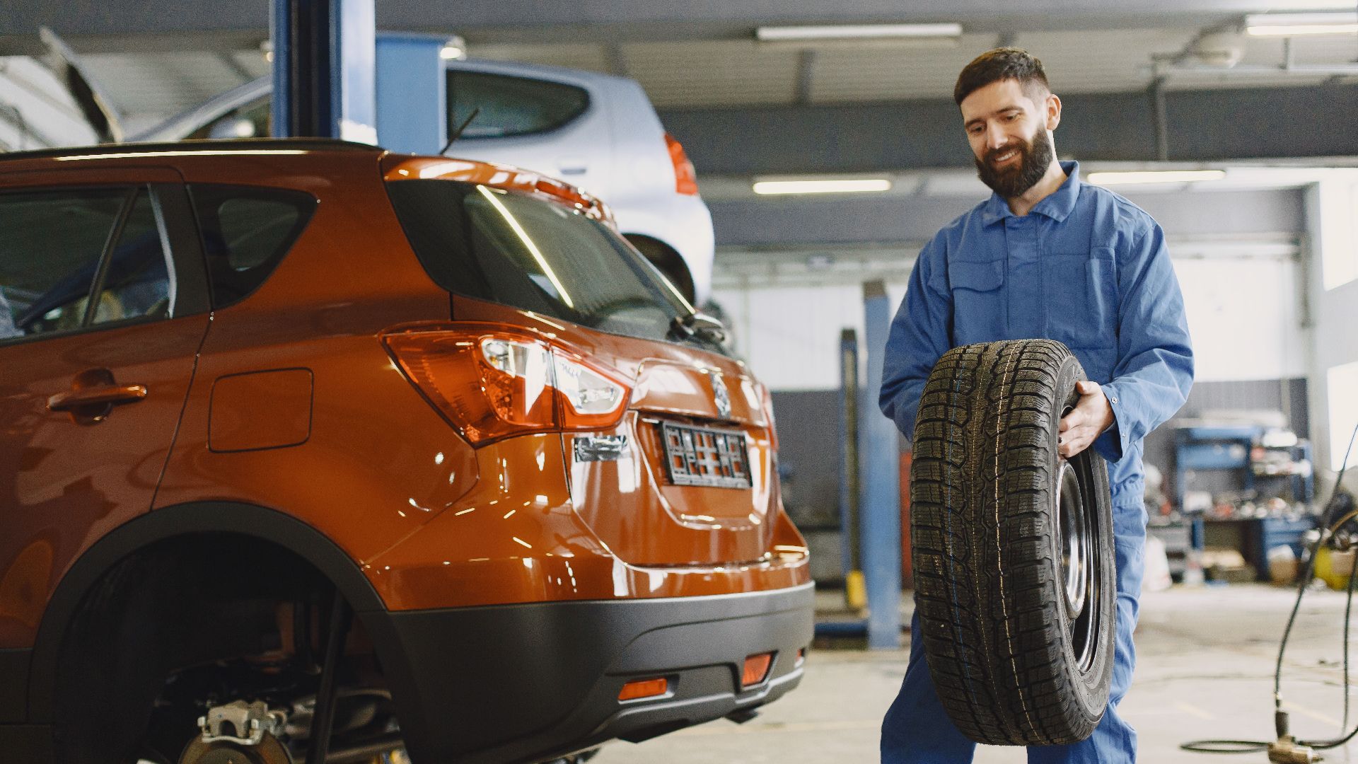 Mechanic holding a tire in a vehicle repair shop, showcasing automotive maintenance.