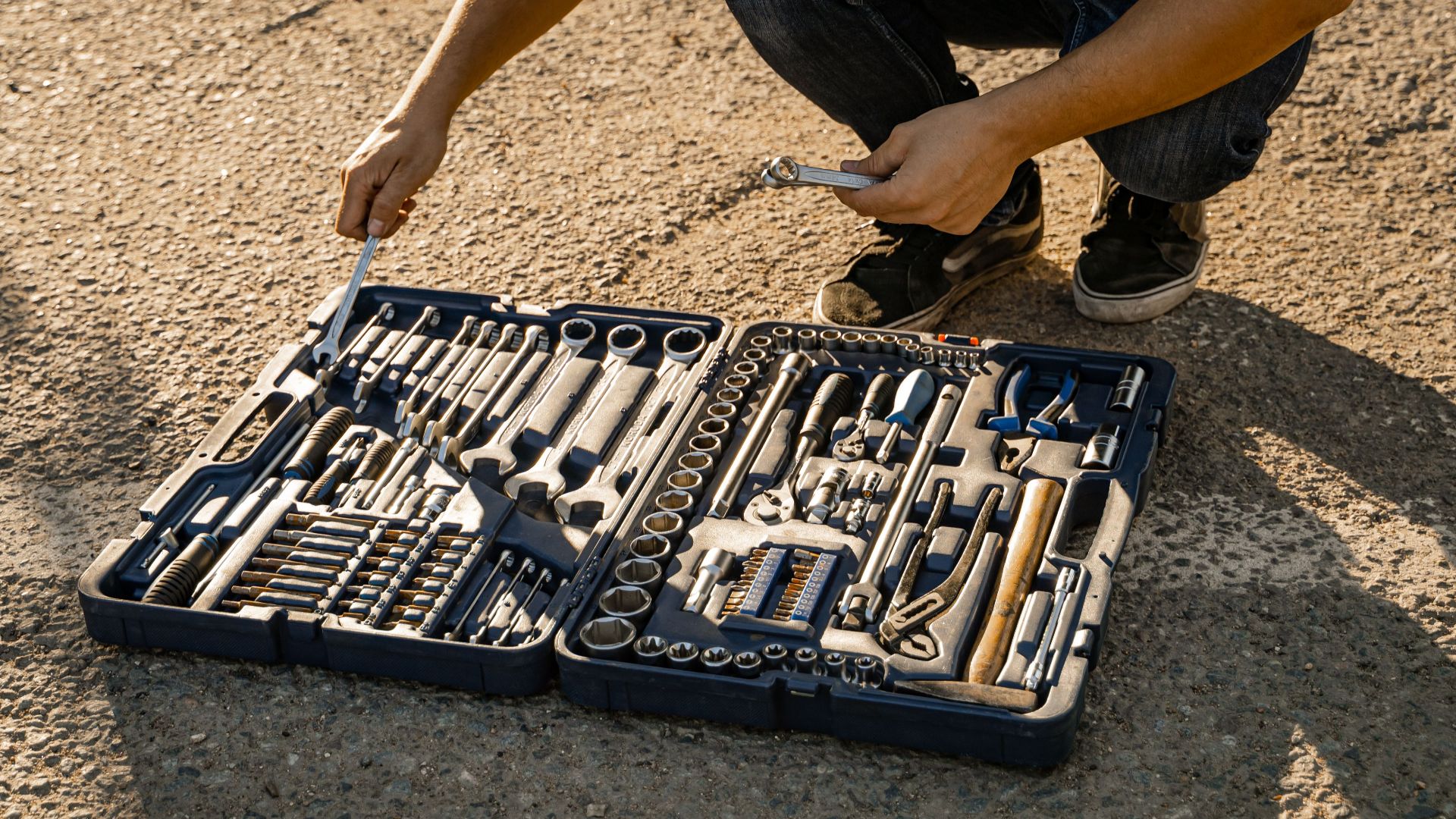Mechanic organizing a toolkit outdoors on a sunny day, highlighting essential hand tools for repair and maintenance.