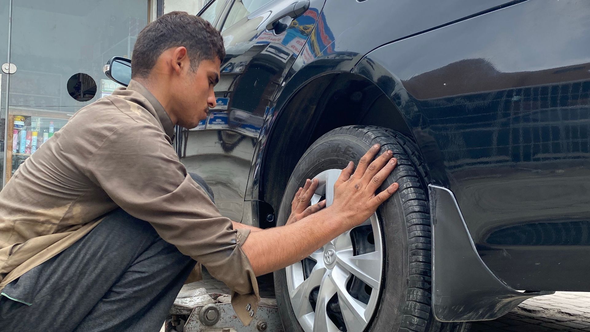 Mechanic carefully attending to tire service on a car at an outdoor service station.