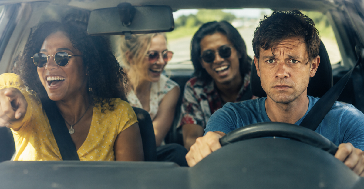 Worried man with a car filled with laughing friends.