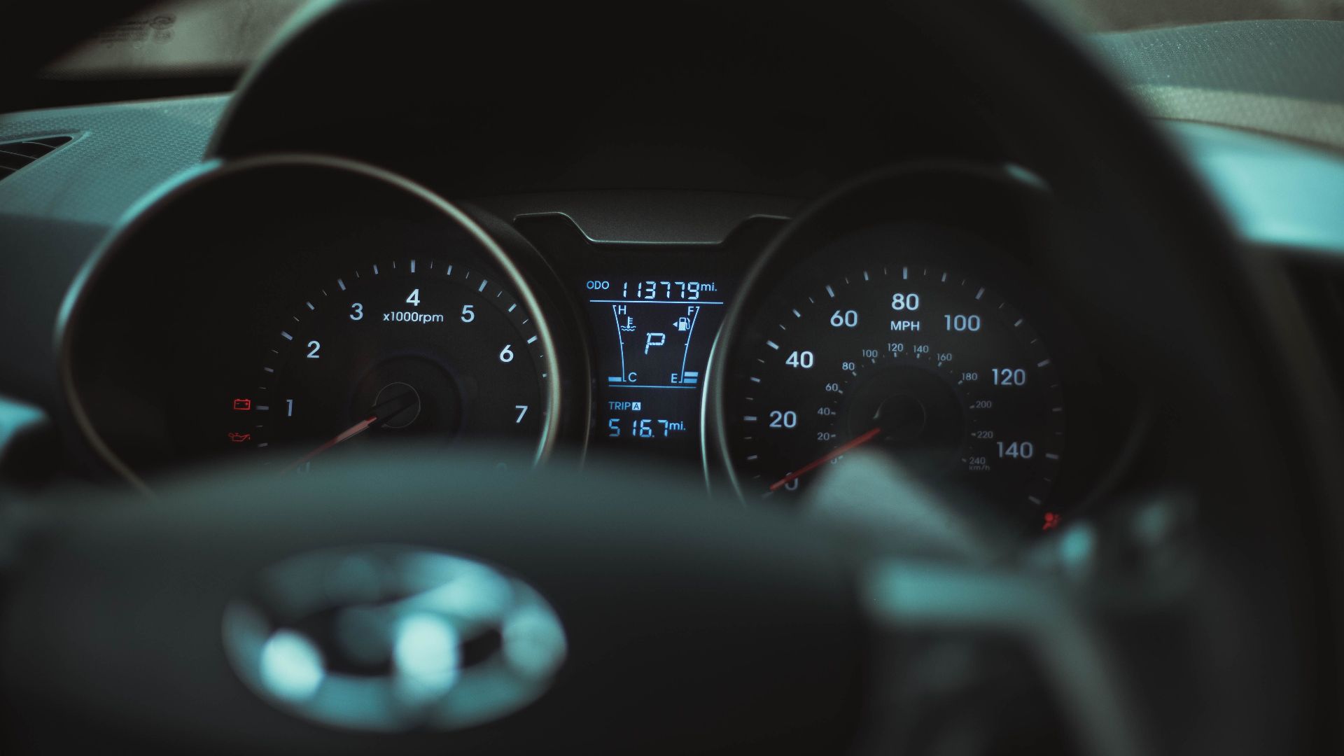 Focus on a car dashboard showing odometer and rev counter in dim light.