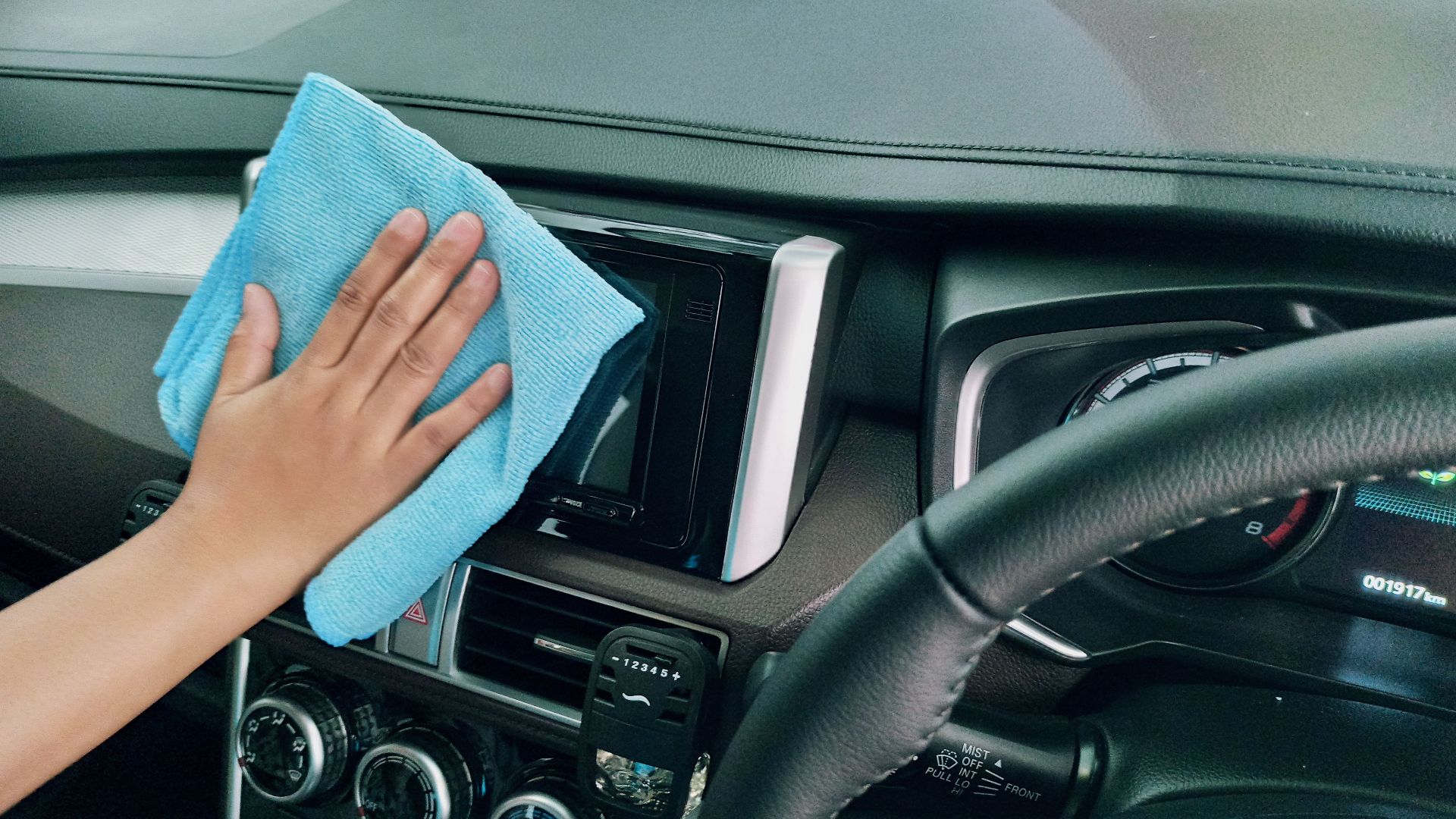 Crop anonymous person polishing panel in right hand drive car by using blue fiber cloth