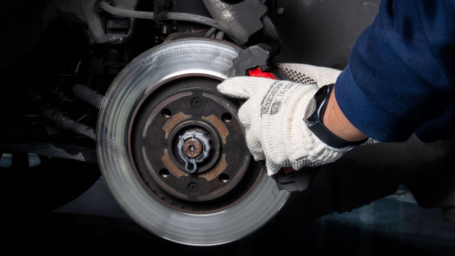 Mechanic working on car brake system in a workshop setting.