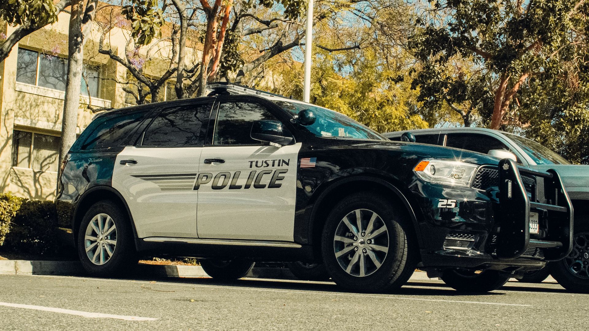 Tustin police car parked in a shaded lot surrounded by trees.