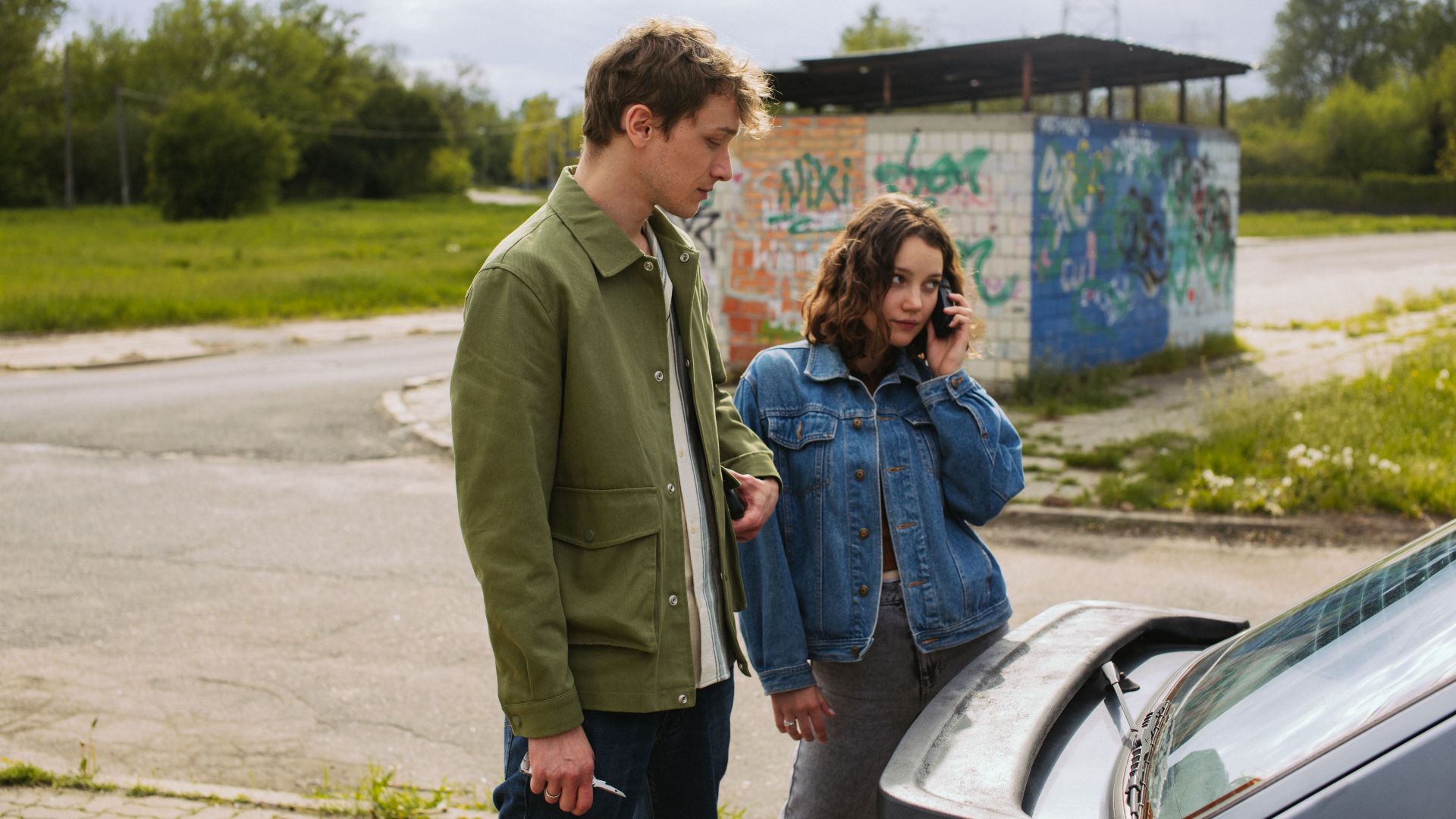 A young couple stands by their car, possibly facing a breakdown.