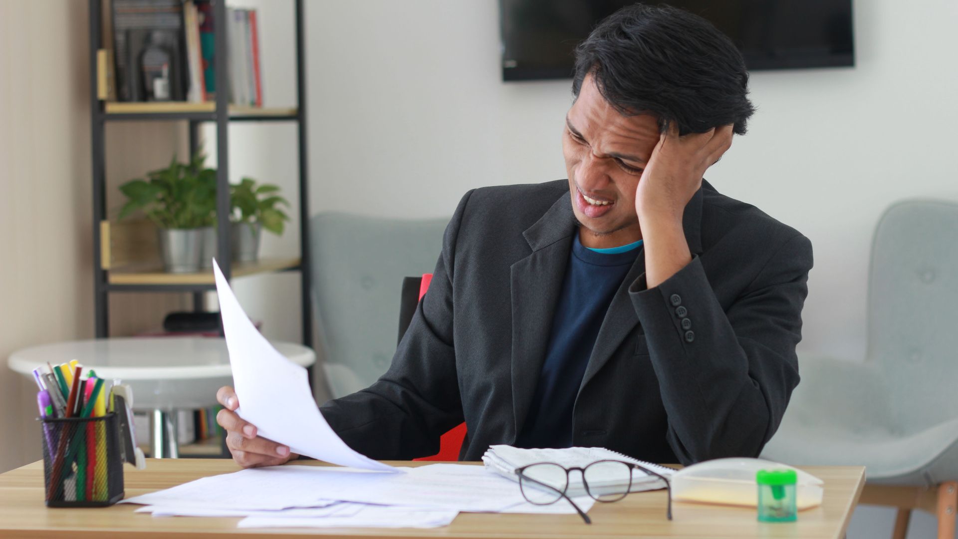 A businessman in an office experiencing stress while reviewing documents.