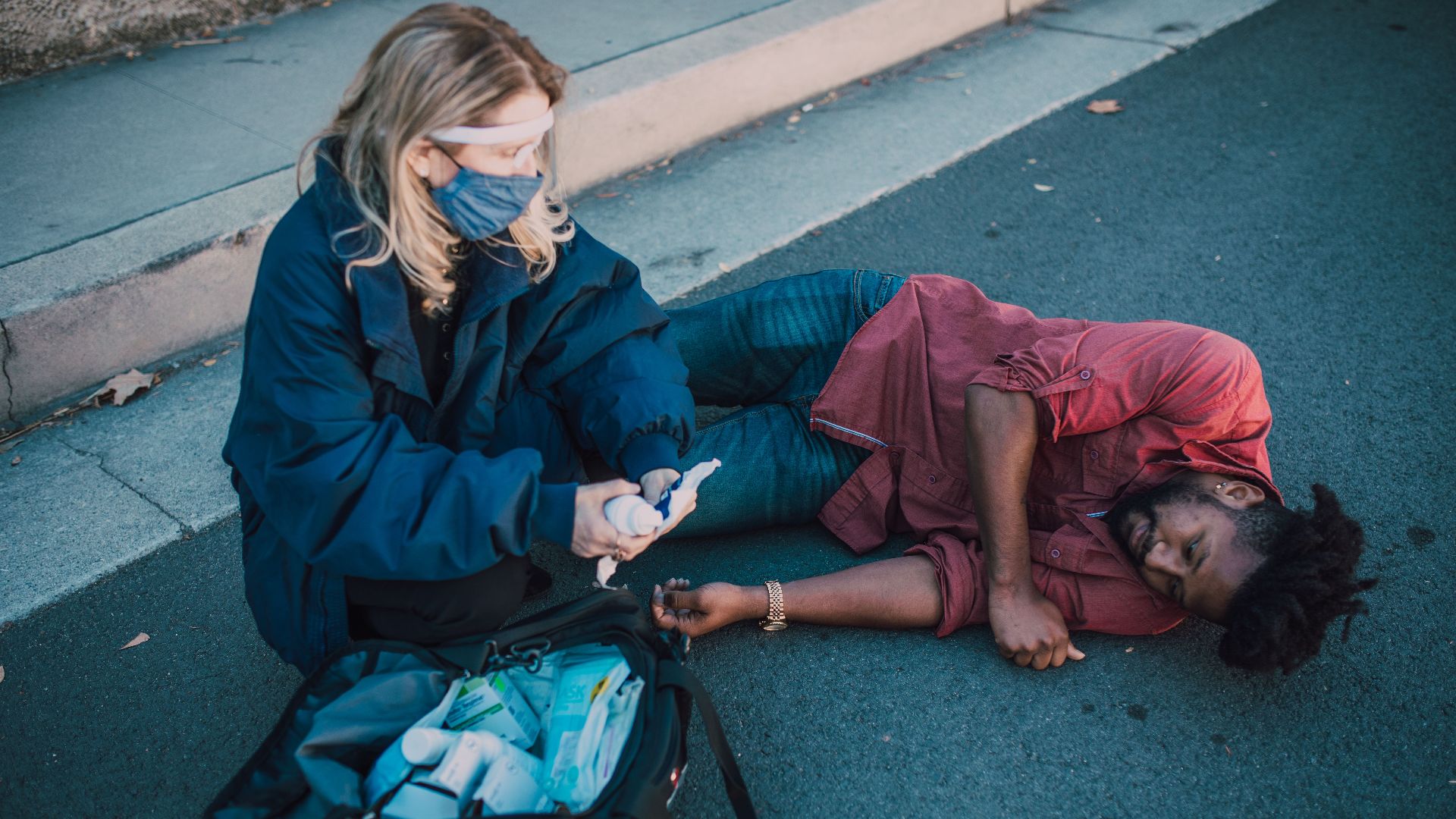 Paramedic provides first aid to injured man lying on roadside.