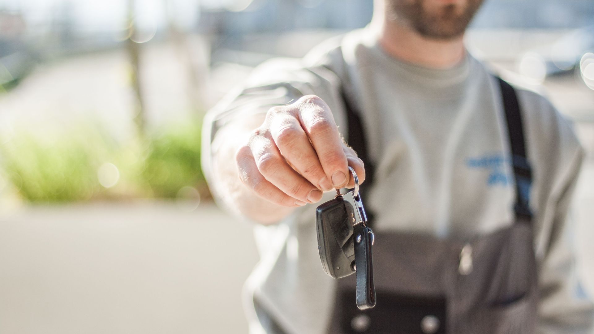 Hand holding a car key outdoors, blurred background, shallow focus.