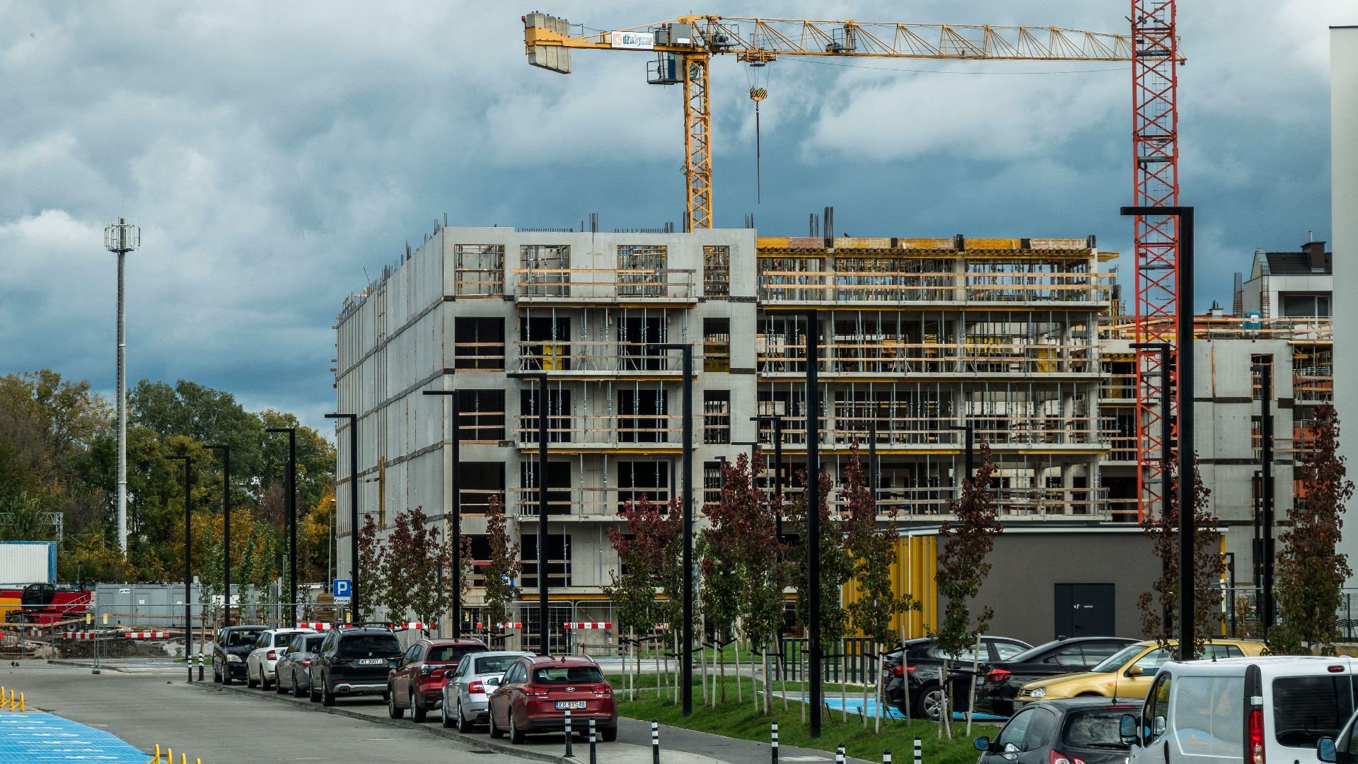A bustling construction site with tower cranes and vehicles under a cloudy sky.