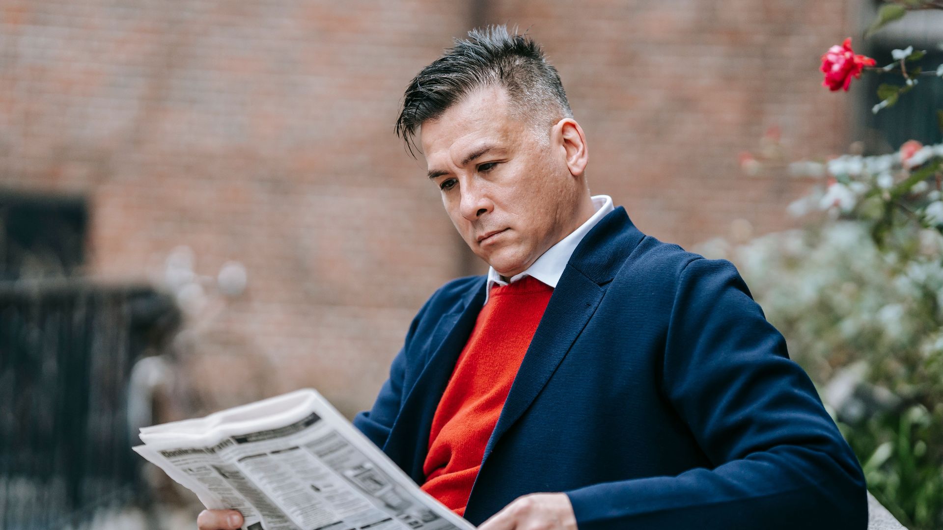 Man reading a newspaper in a stylish outfit, enjoying a relaxed moment outdoors.