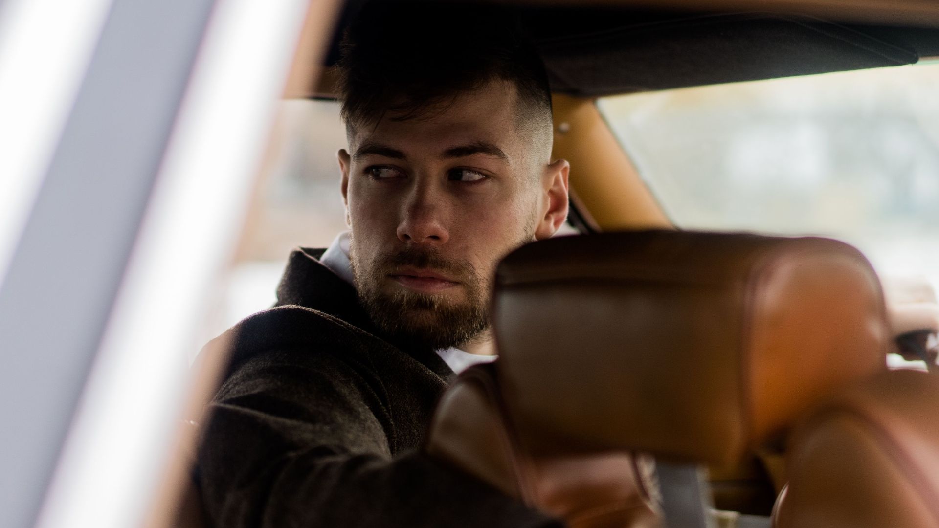 Confident adult male driver in elegant outfit sitting in vehicle while looking in back window on street in daytime