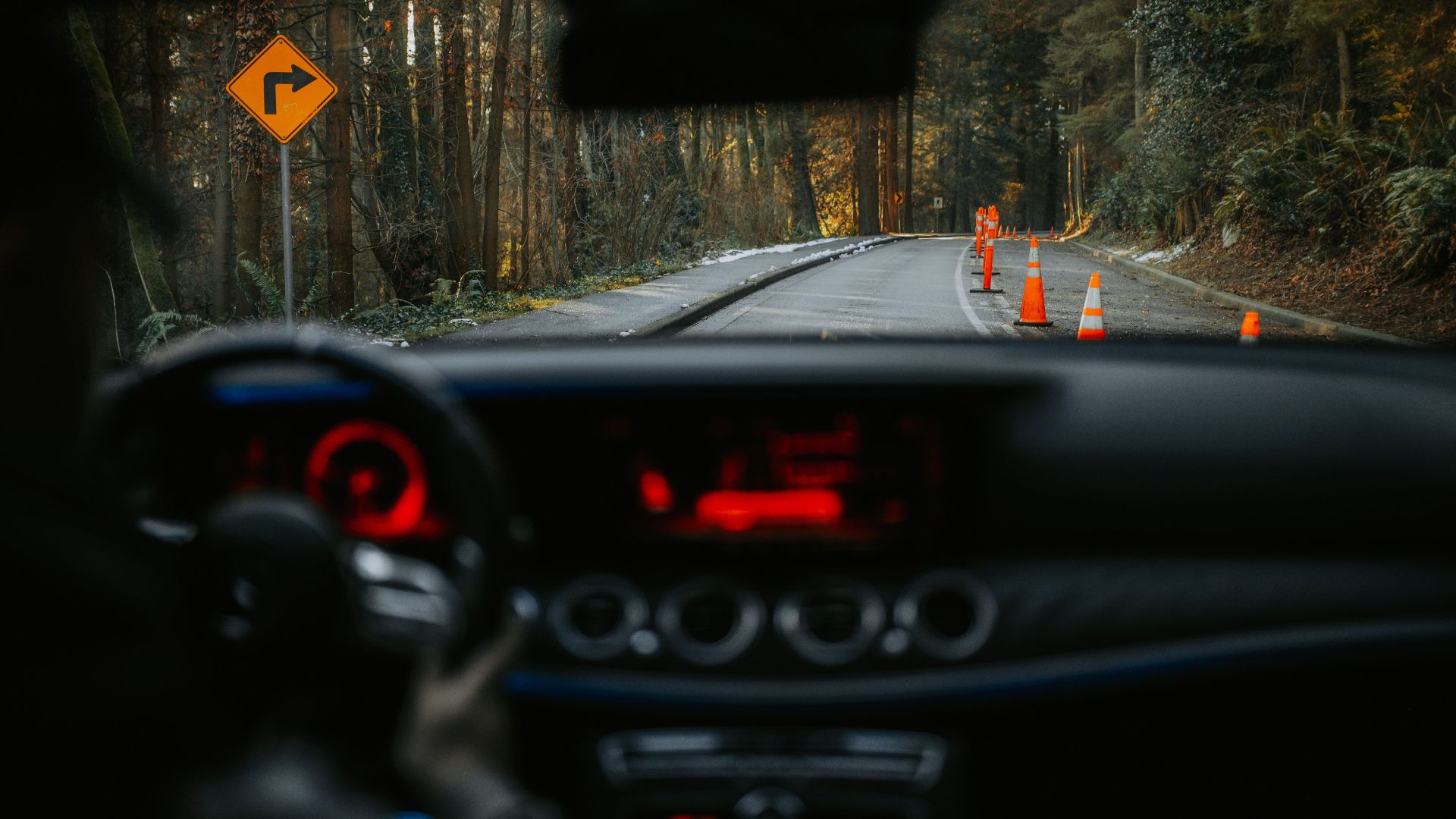 View from car dashboard of rural road with traffic cones and turn sign. Scenic forest driving experience.