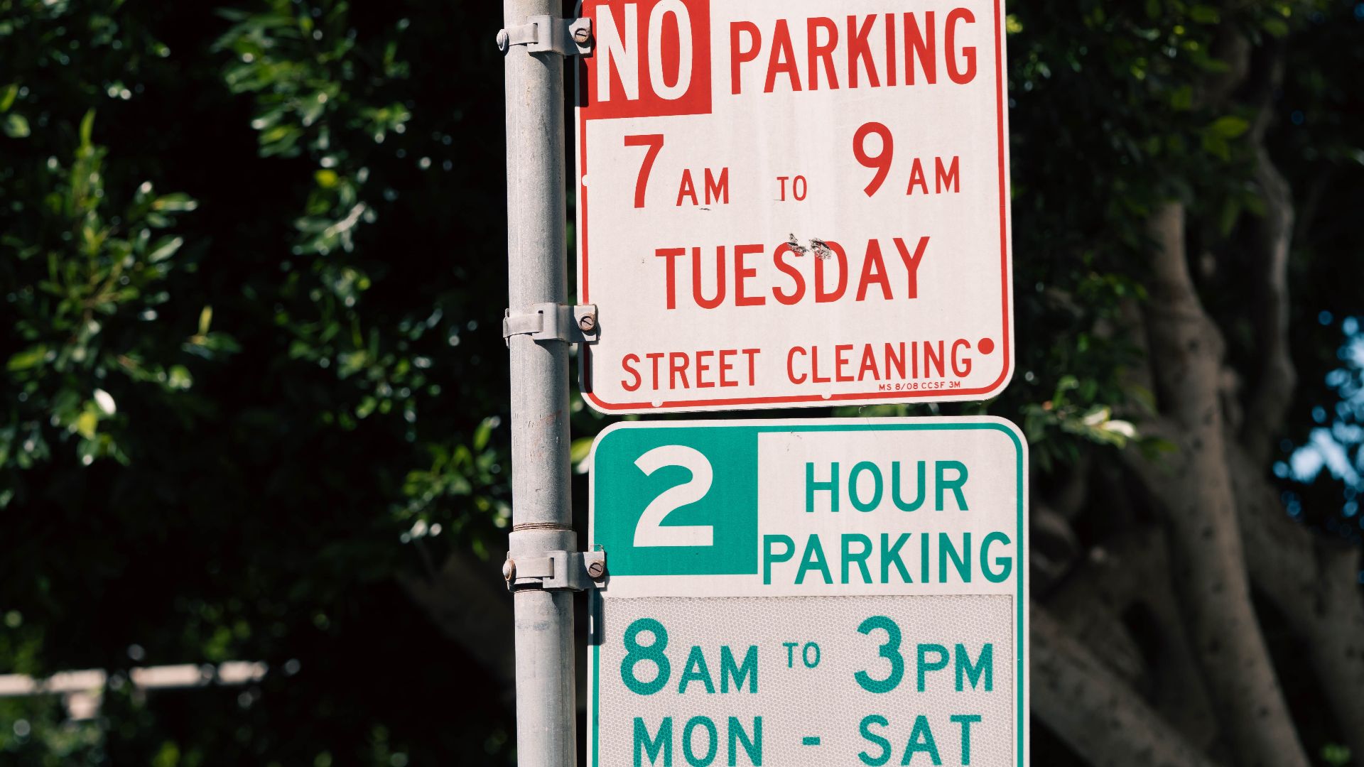 Street parking signs displaying timing and rules in a shaded urban area.