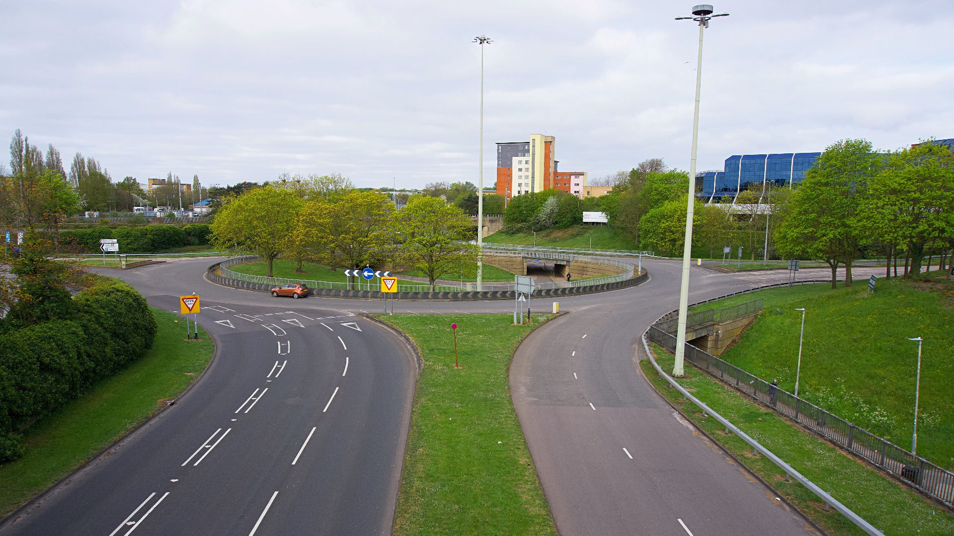 Roundabout with clear road markings surrounded by greenery and buildings in the background.