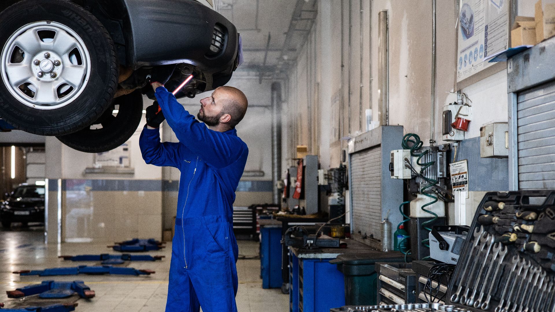 Mechanic inspecting a raised car in an auto workshop for maintenance and repair services.