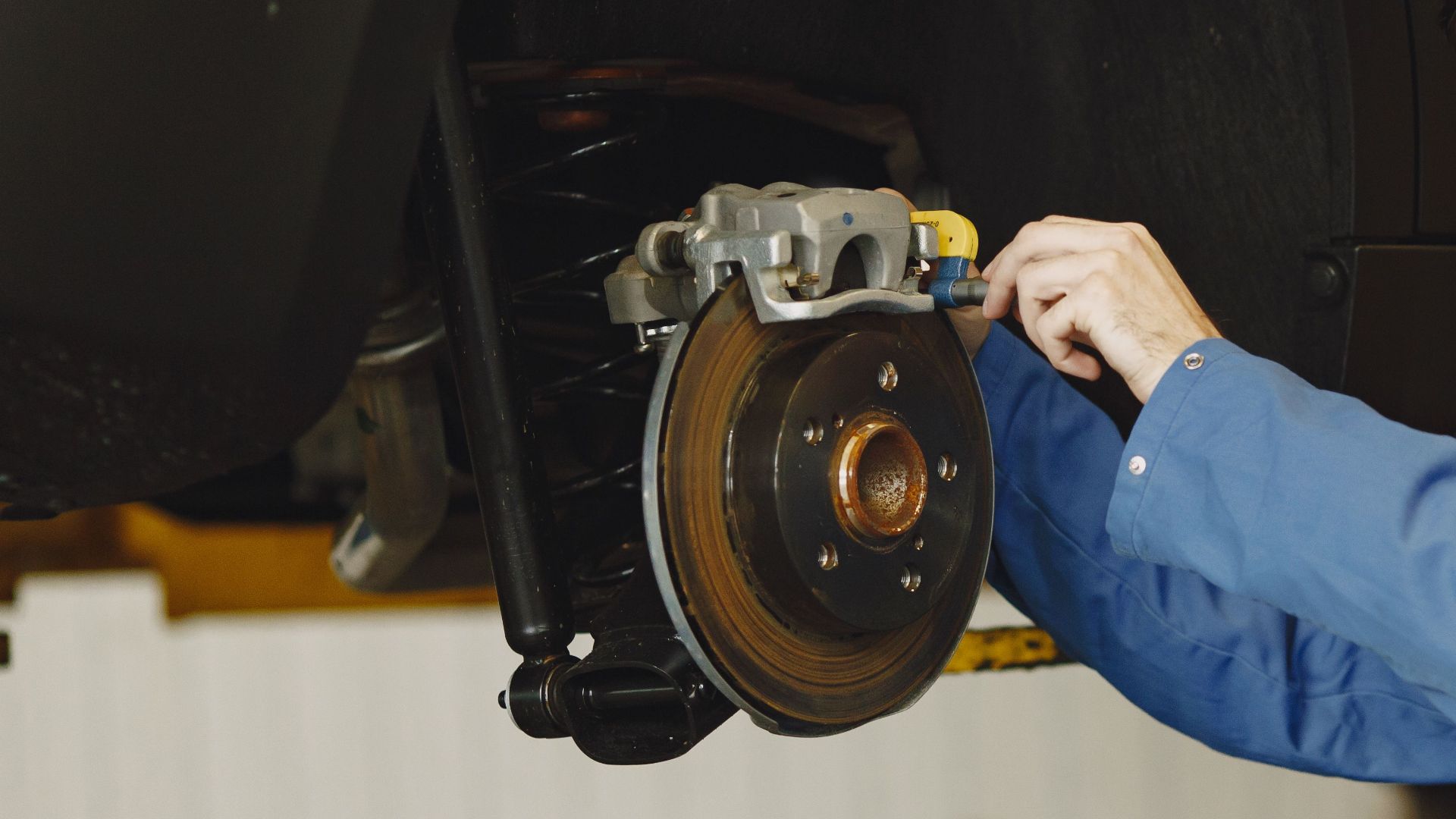 Mechanic in blue uniform performing brake repair on car in modern garage.