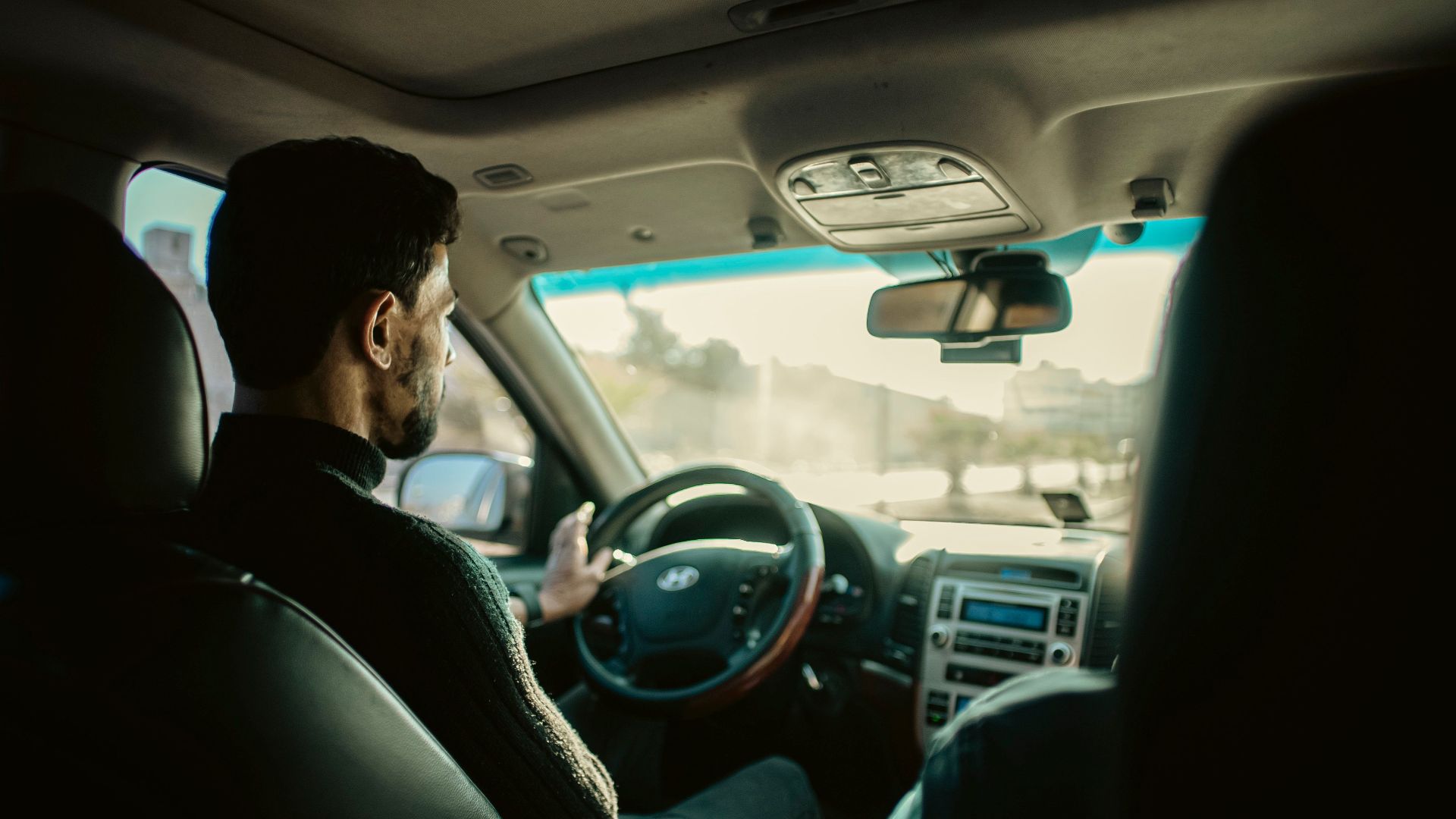 Man driving through city streets of Manbij, Aleppo, in a modern sedan.