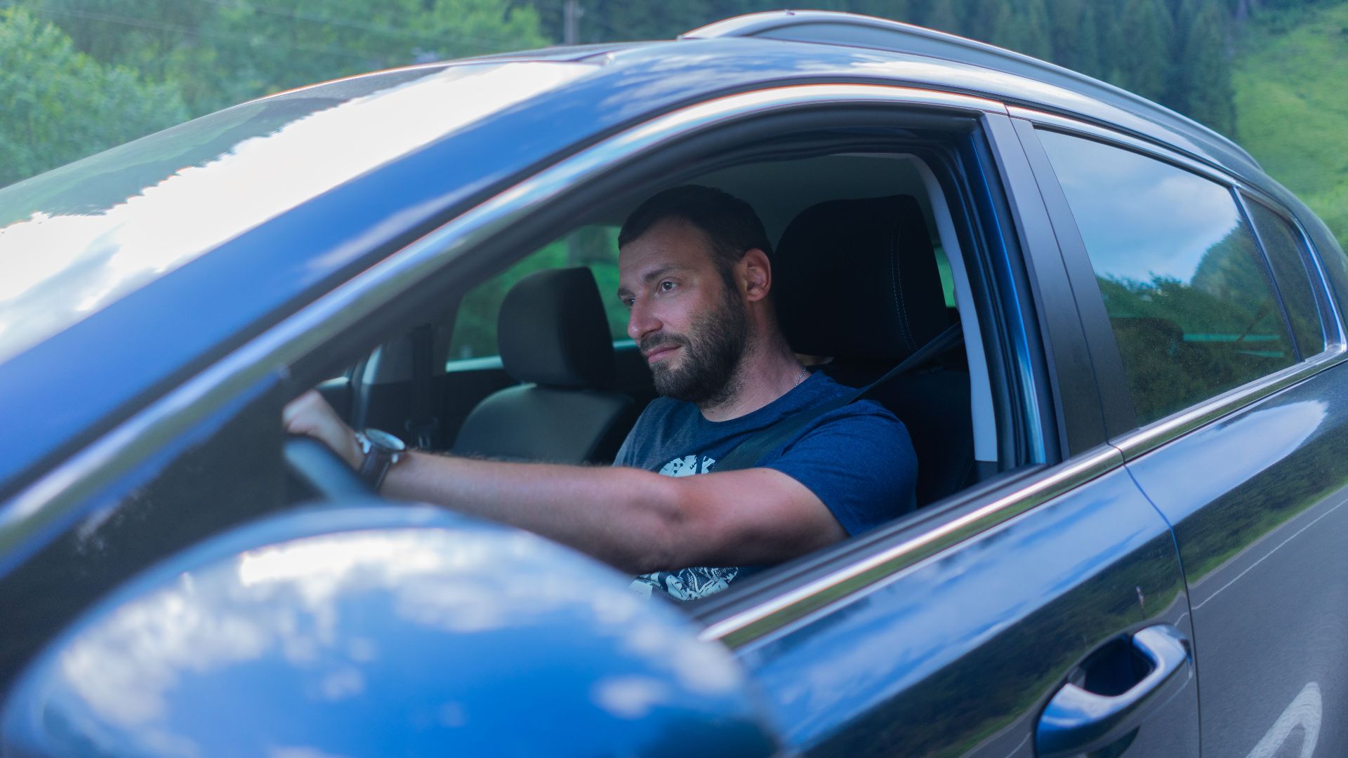 Bearded man enjoying a drive through lush green countryside on a sunny day.