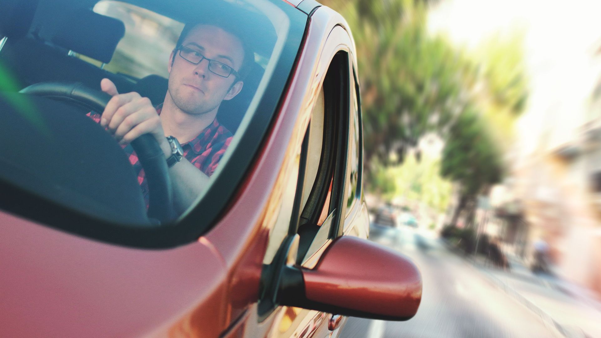 A man driving fast through a city street in a red car, showcasing motion and focus.