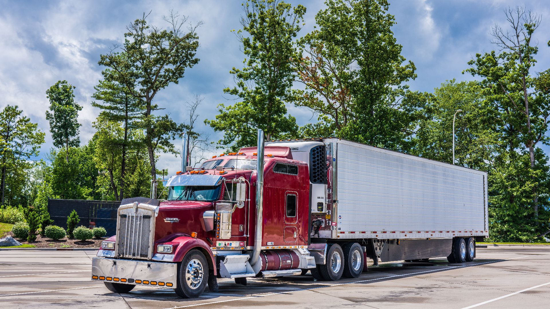 A striking red semi truck parked in a lush scenic area, showcasing modern transportation technology.