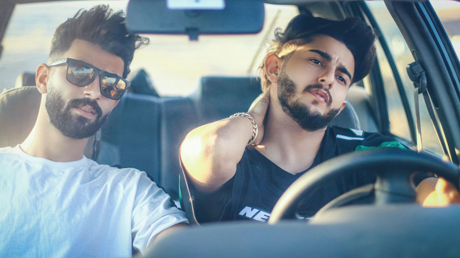 Two bearded men enjoy a drive, relaxing inside a parked car during the day.