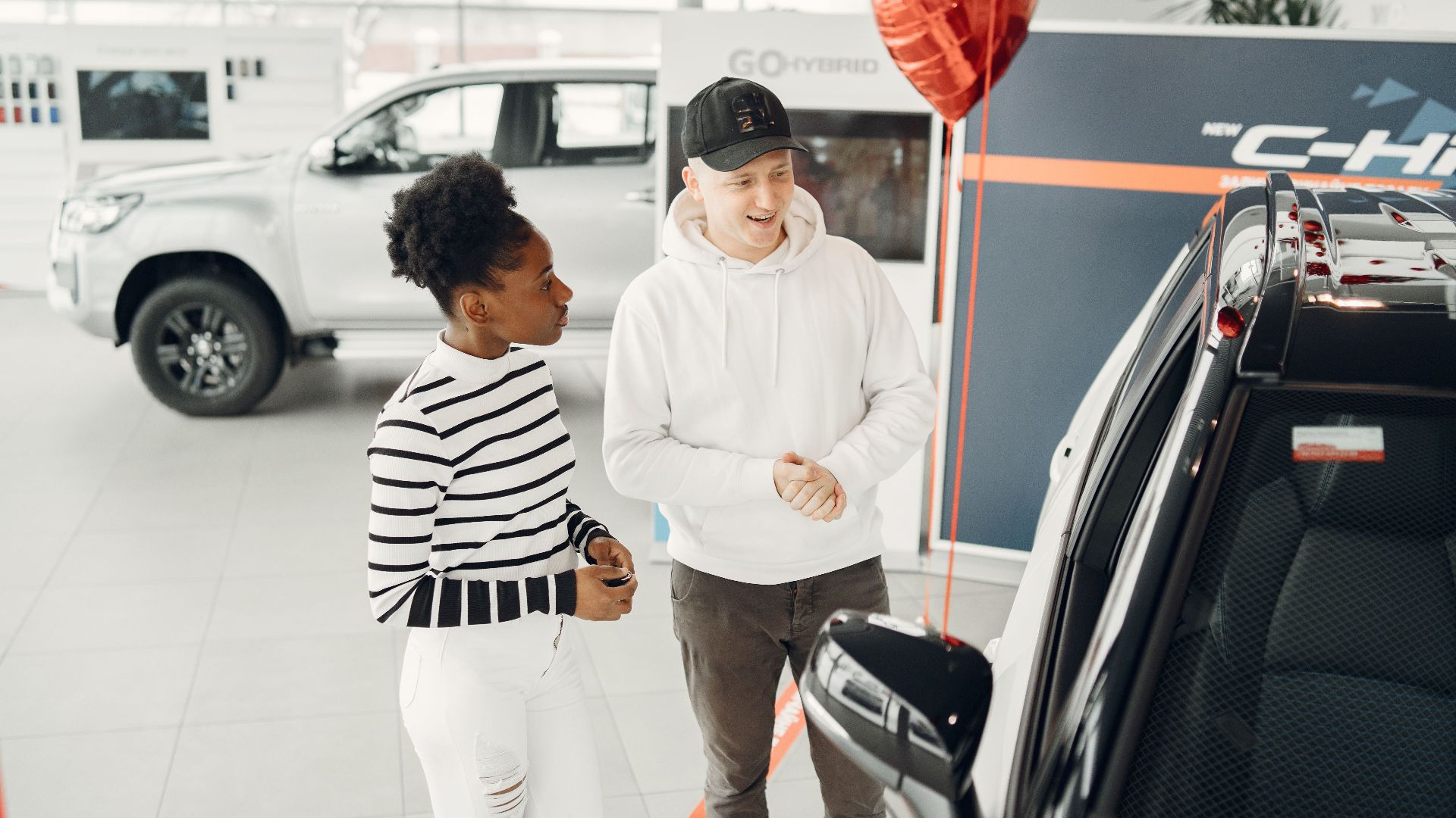 A young couple examines cars in a modern dealership showroom, highlighting customer experience.