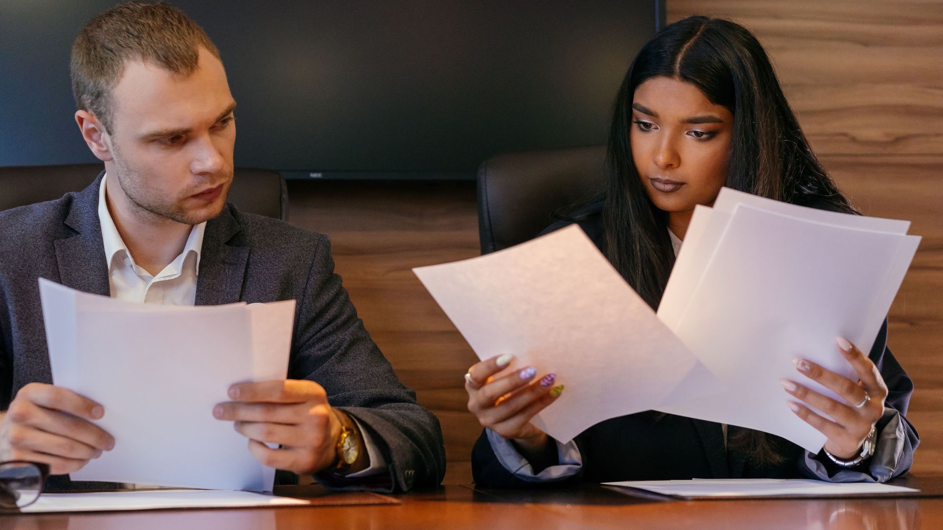 Two diverse professionals reviewing documents in a modern office setting, showcasing teamwork and focus.
