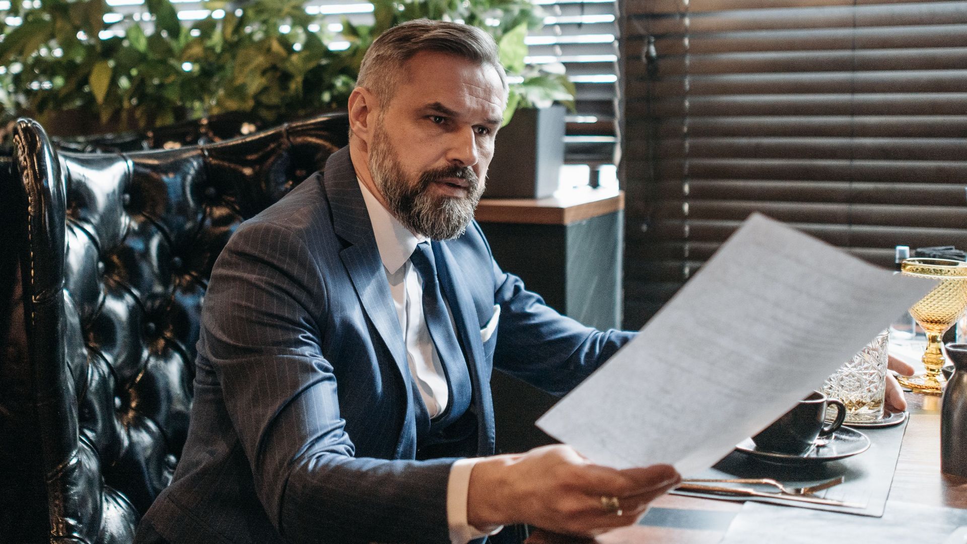 Elderly businessman in a suit analyzing paperwork in a modern office with plants.
