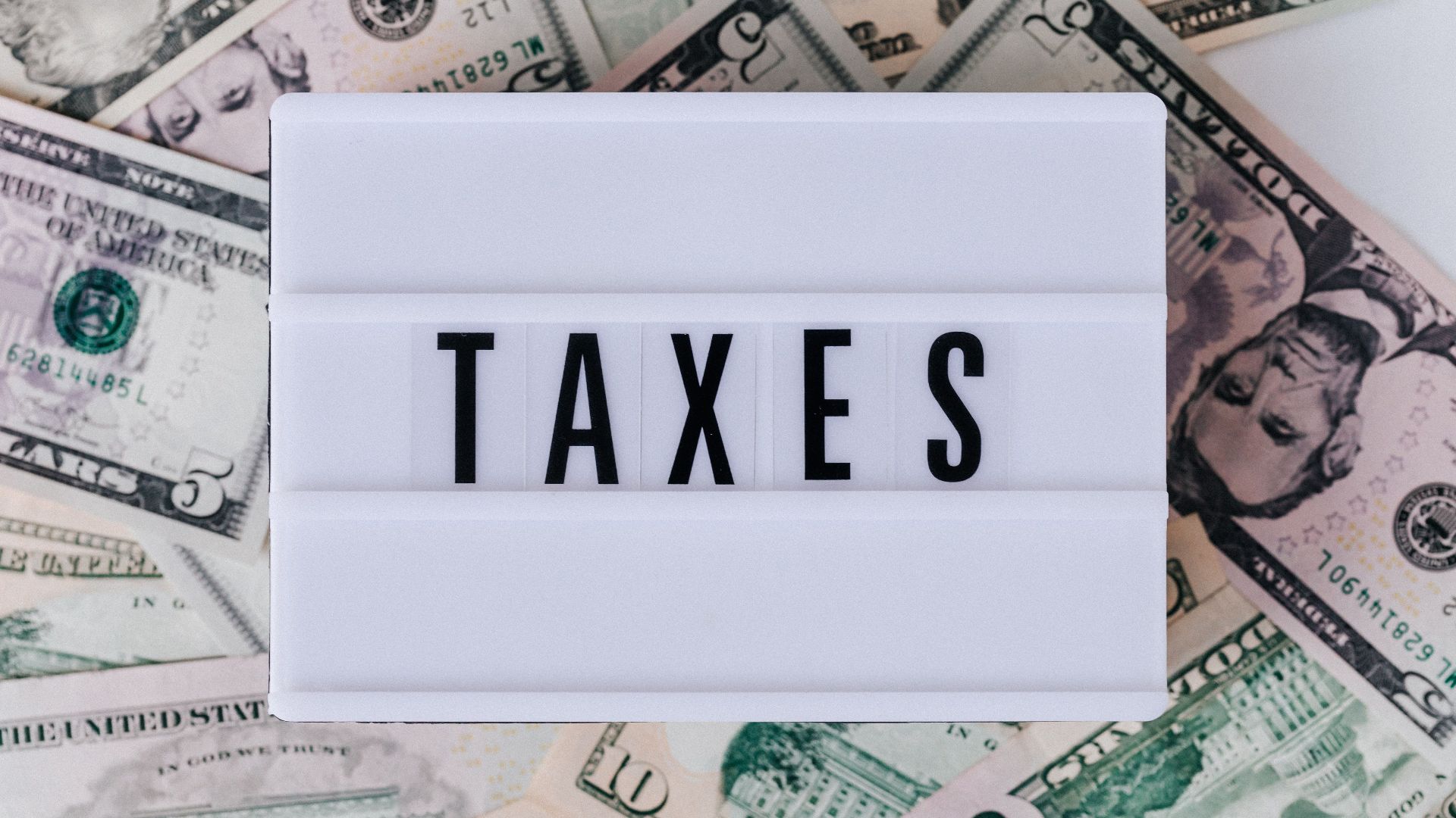 Top view of white vintage light box with TAXES inscription placed on stack of USA dollar bills on white surface