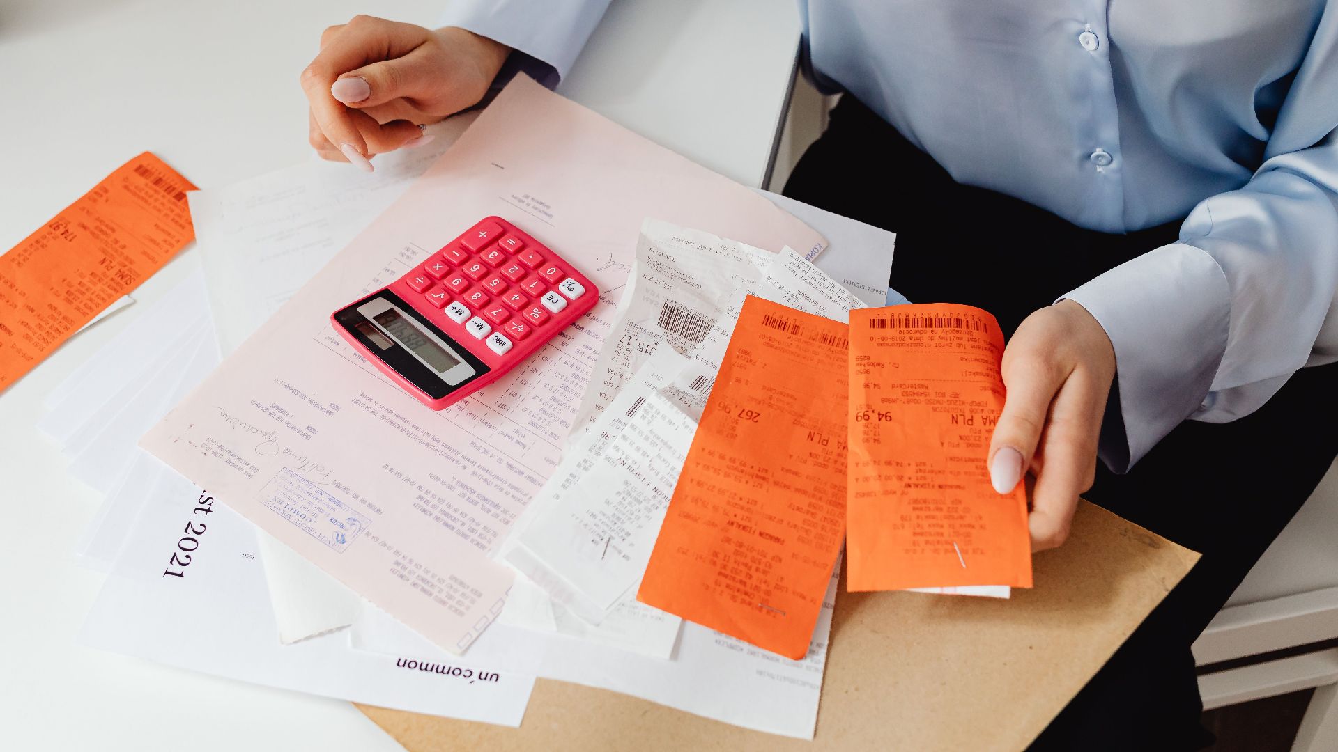 A woman reviews receipts and calculates expenses at a desk with a pink calculator.