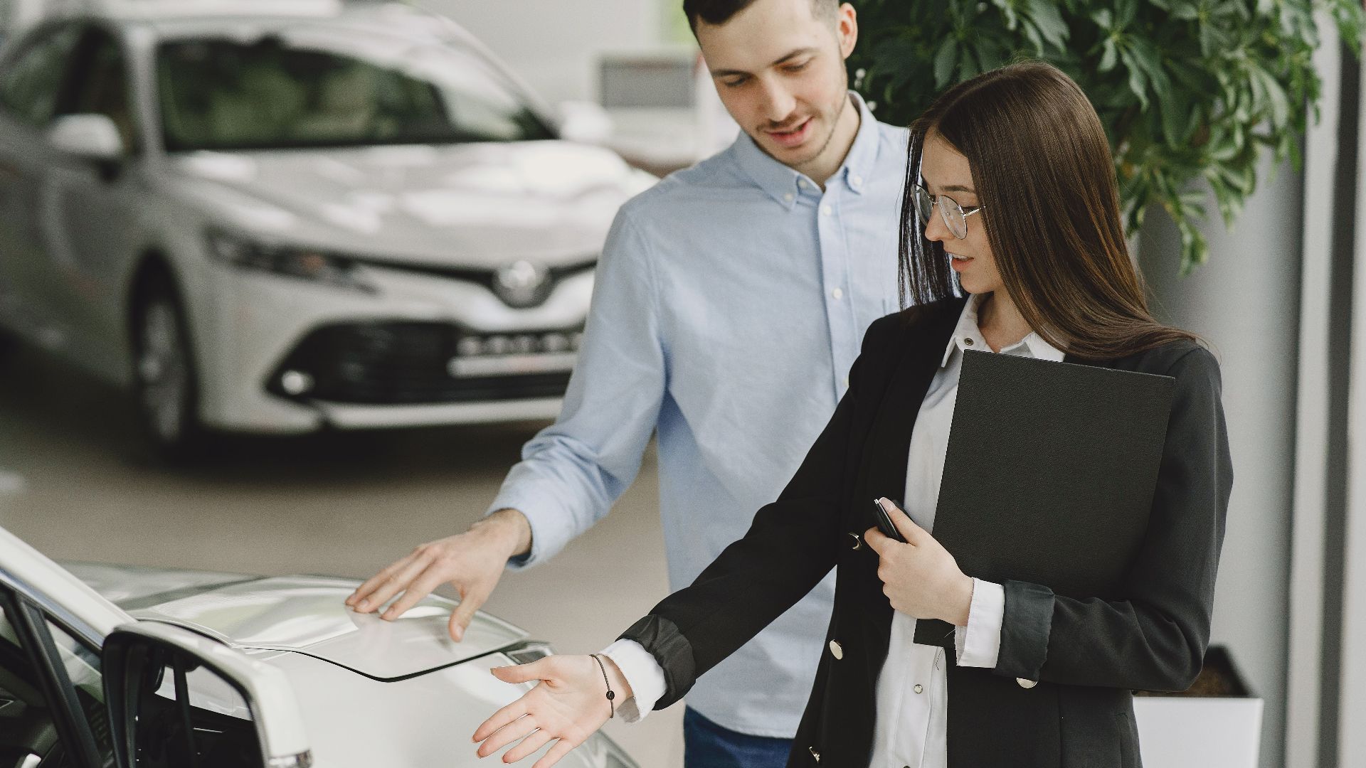 A man and saleswoman discussing a hybrid vehicle's features in an indoor showroom.