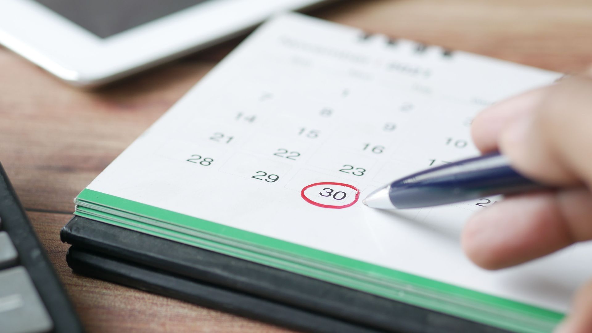 Close-up shot of a hand marking a date on a calendar with a pen, emphasizing planning and scheduling.