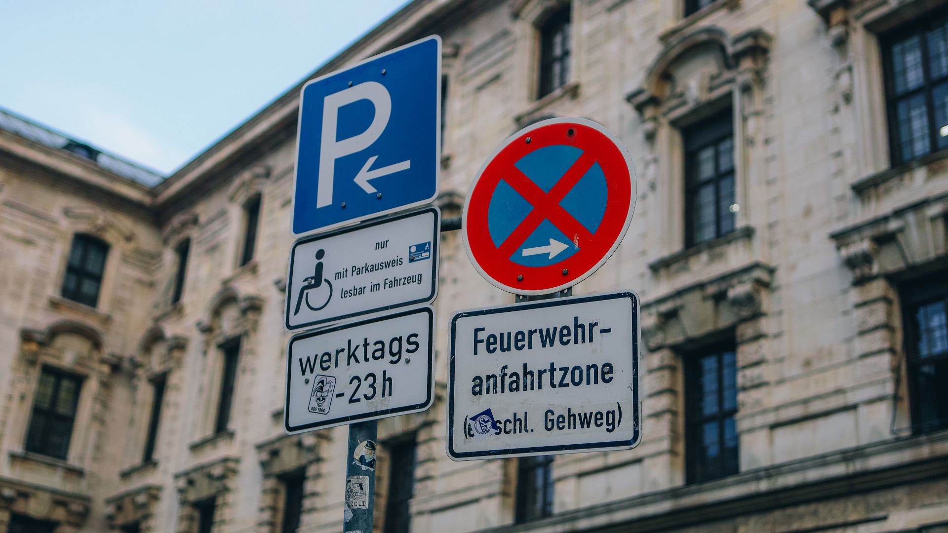 Street signs in front of traditional building facade in urban setting, featuring no parking zone.