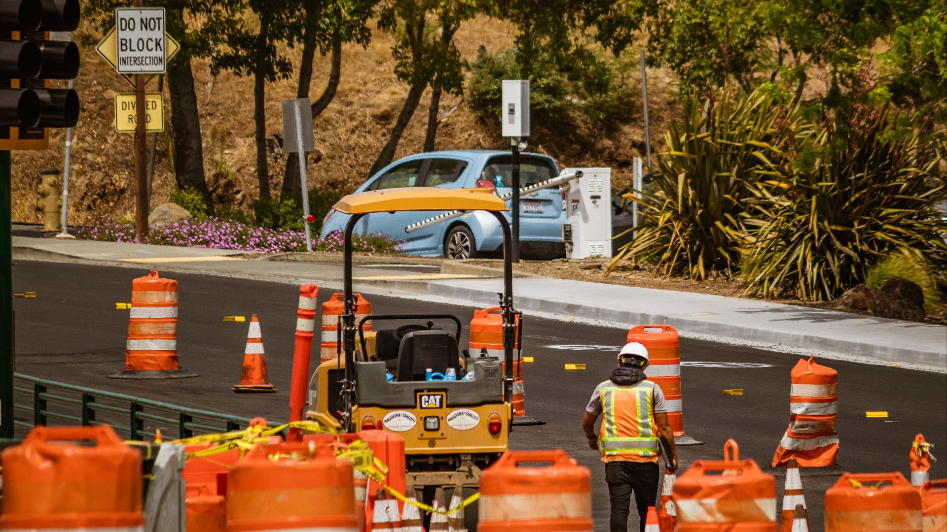 A road construction worker surrounded by safety cones on a street in daylight.