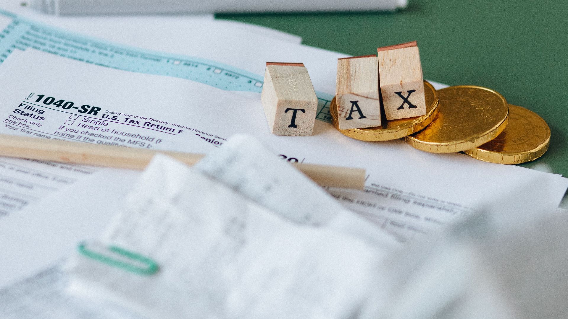 Tax forms, coins, and block letters spelling 'TAX' on a green background, symbolizing finance.
