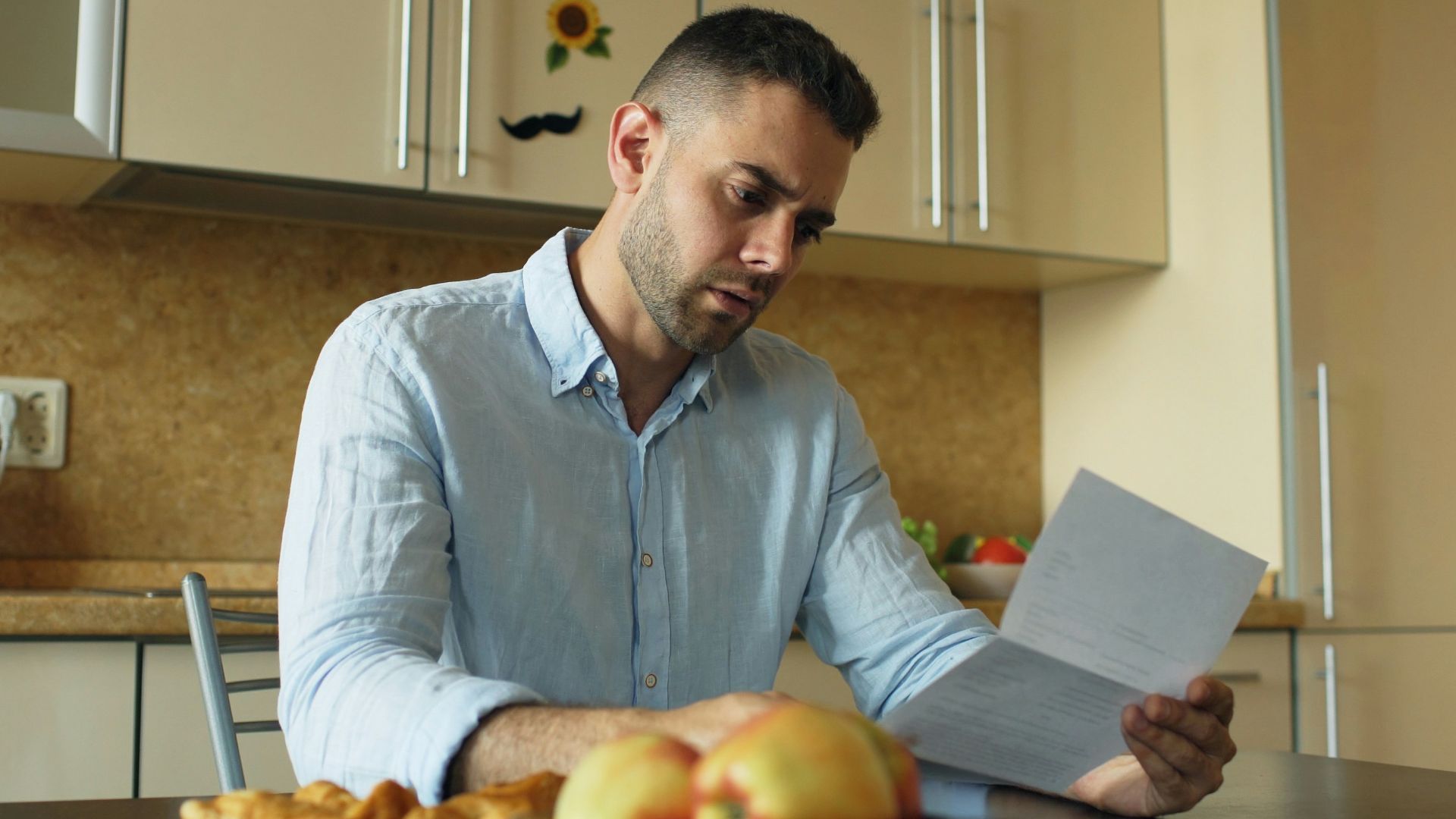 Man reading document at kitchen table with fruit and fruit