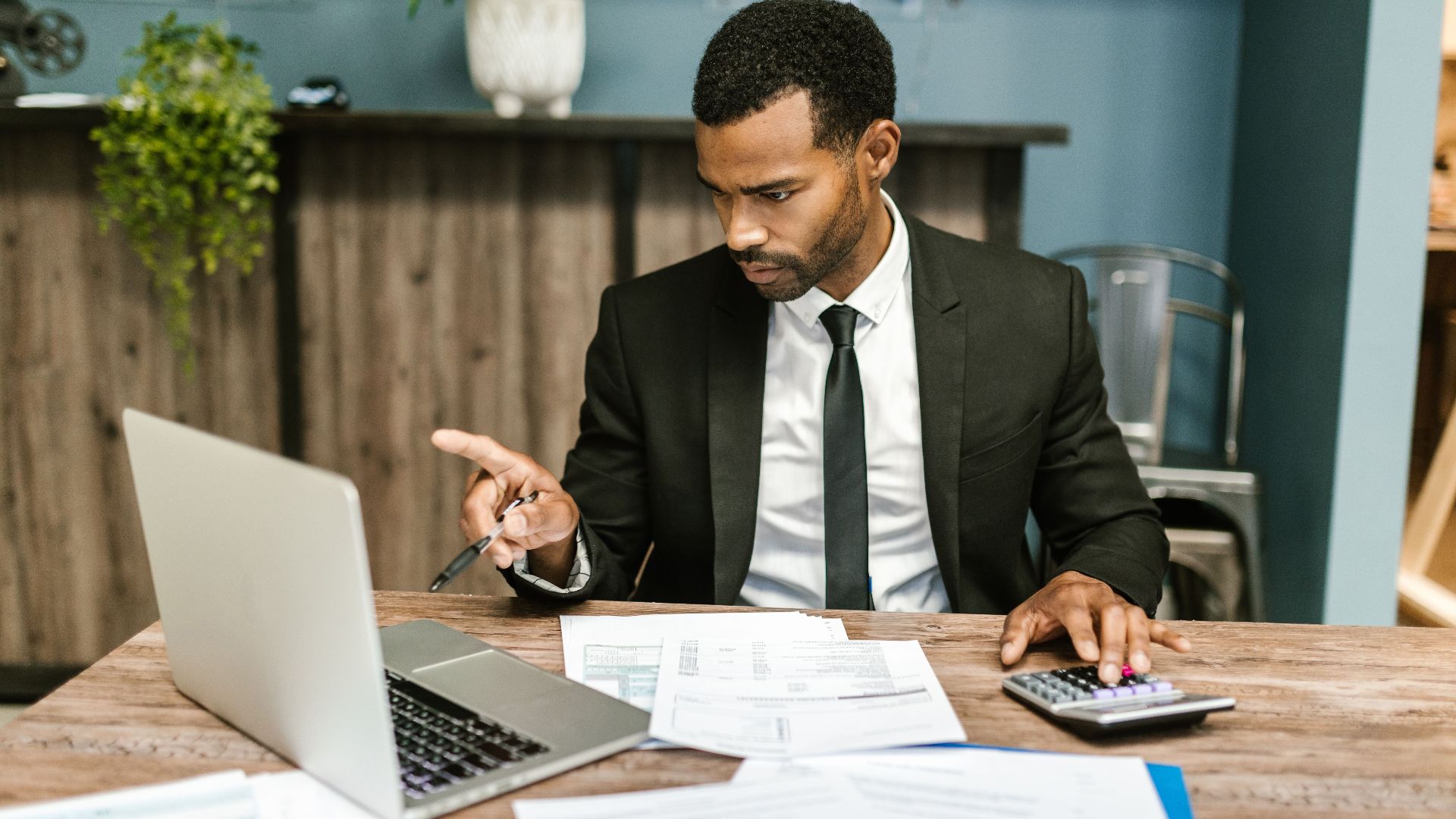 Professional man in a suit using a laptop and calculator in an office setting.
