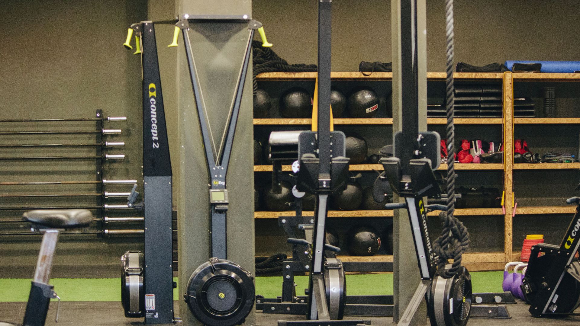 Modern gym with exercise equipment including rowing and ski machines, weights, and ropes.