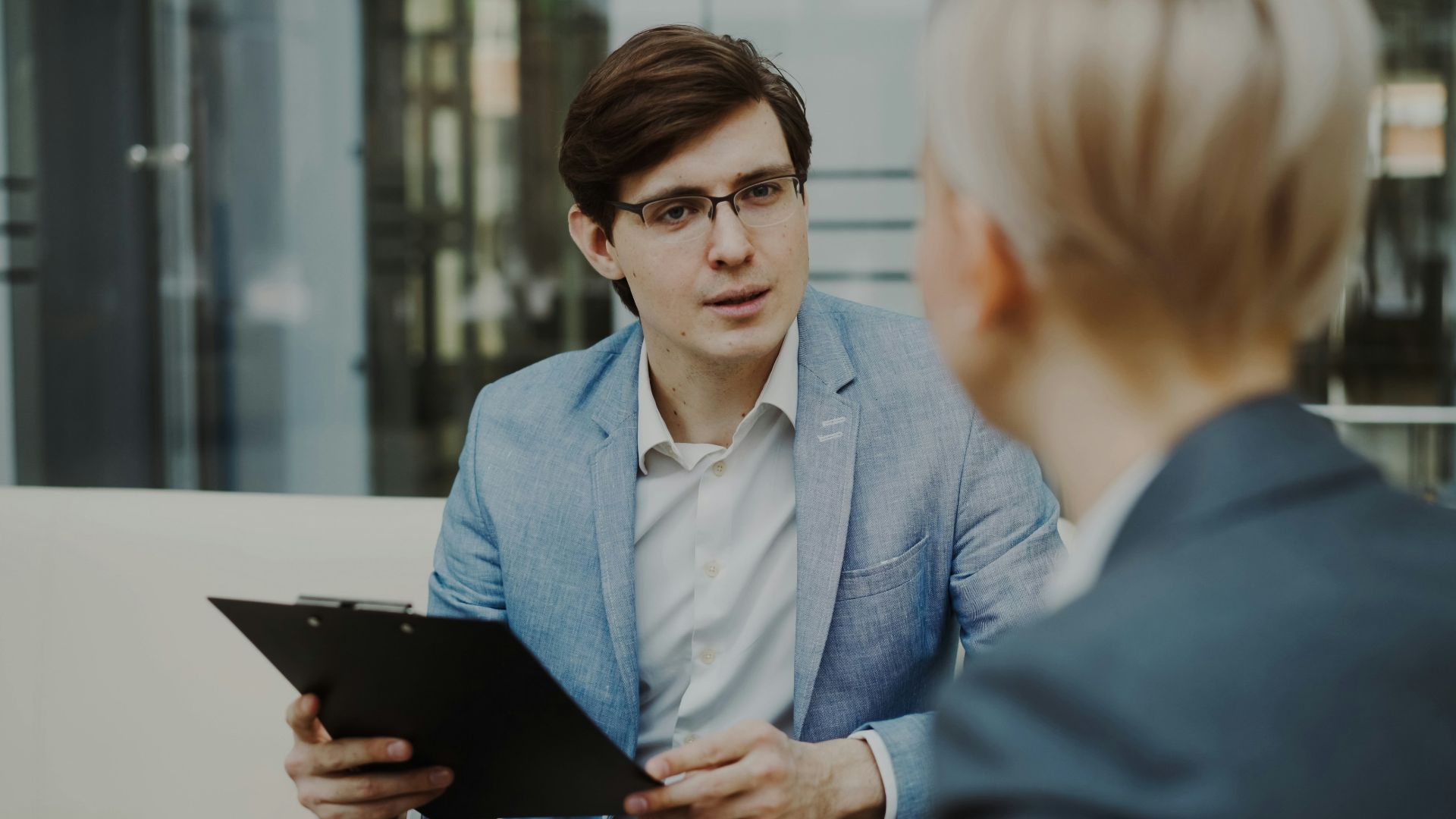 Man in suit holding clipboard talking to woman